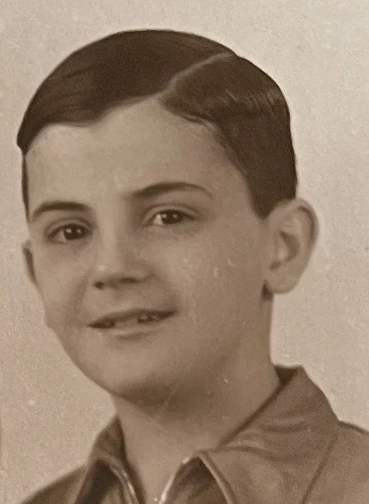 Black and white photograph of a young boy with short, dark, slicked-back hair wearing a collared jacket.
