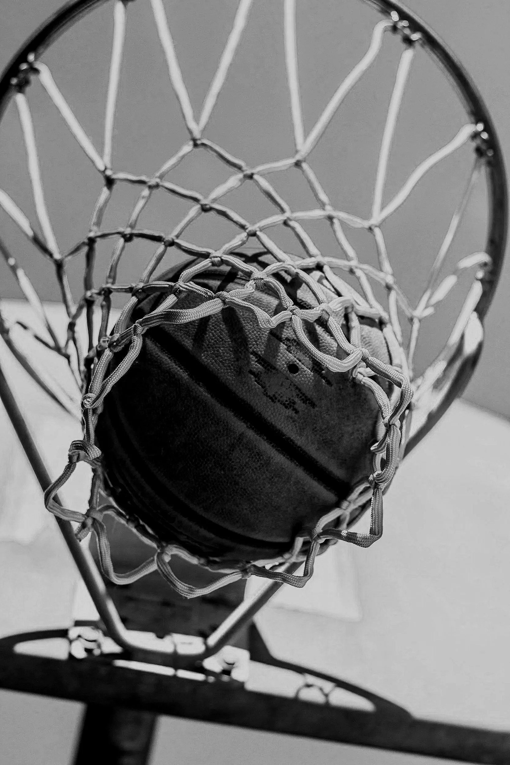 Black and white photo of a basketball hoop with a basketball stuck in the net.