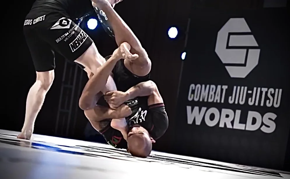 Two male athletes competing in a Brazilian Jiu-Jitsu match at the Combat Jiu-Jitsu Worlds event, with one executing a choke hold on the other.
