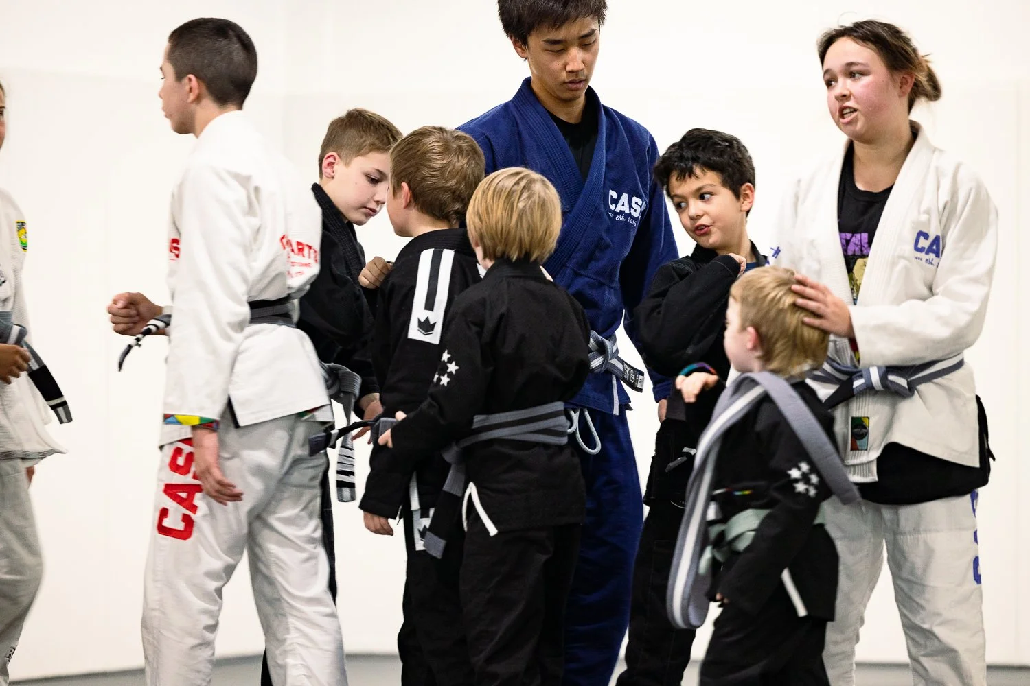 A group of children and an adult in judo uniforms, gathered in a dojo, engaged in a judo class or training session.