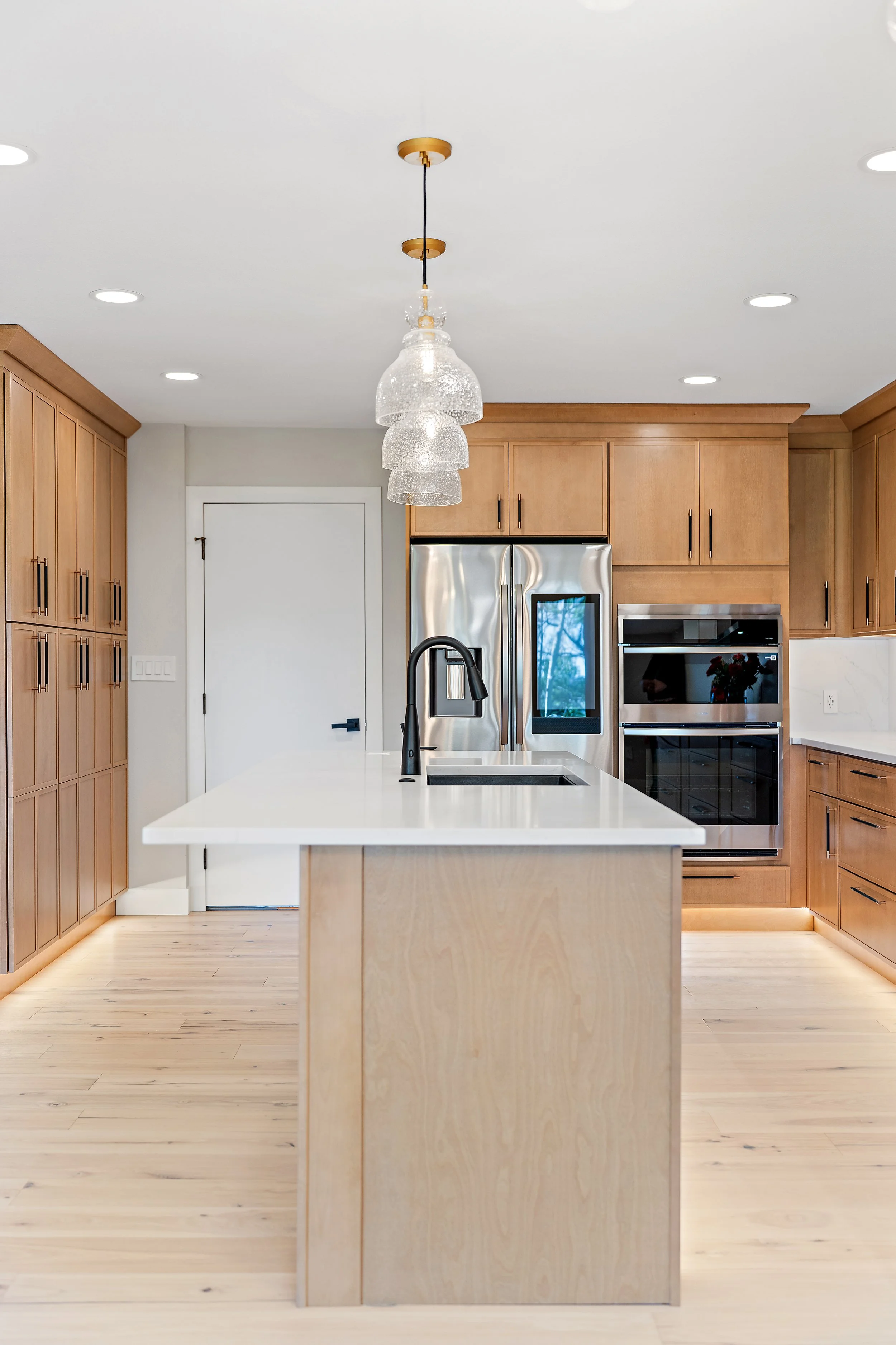 Modern kitchen with wooden cabinets, stainless steel appliances, and a white island with a black faucet. A pendant light fixture hangs from the ceiling.