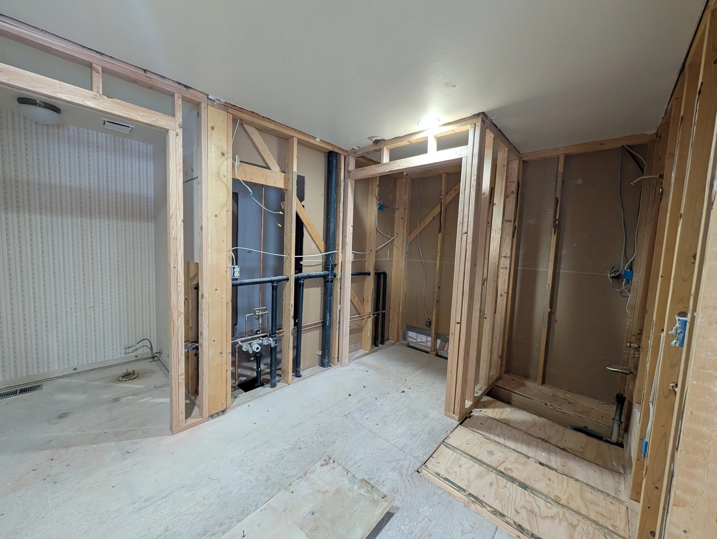 Interior of a house under renovation, showing exposed wooden framing and plumbing, with drywall partially installed on the ceiling and walls.