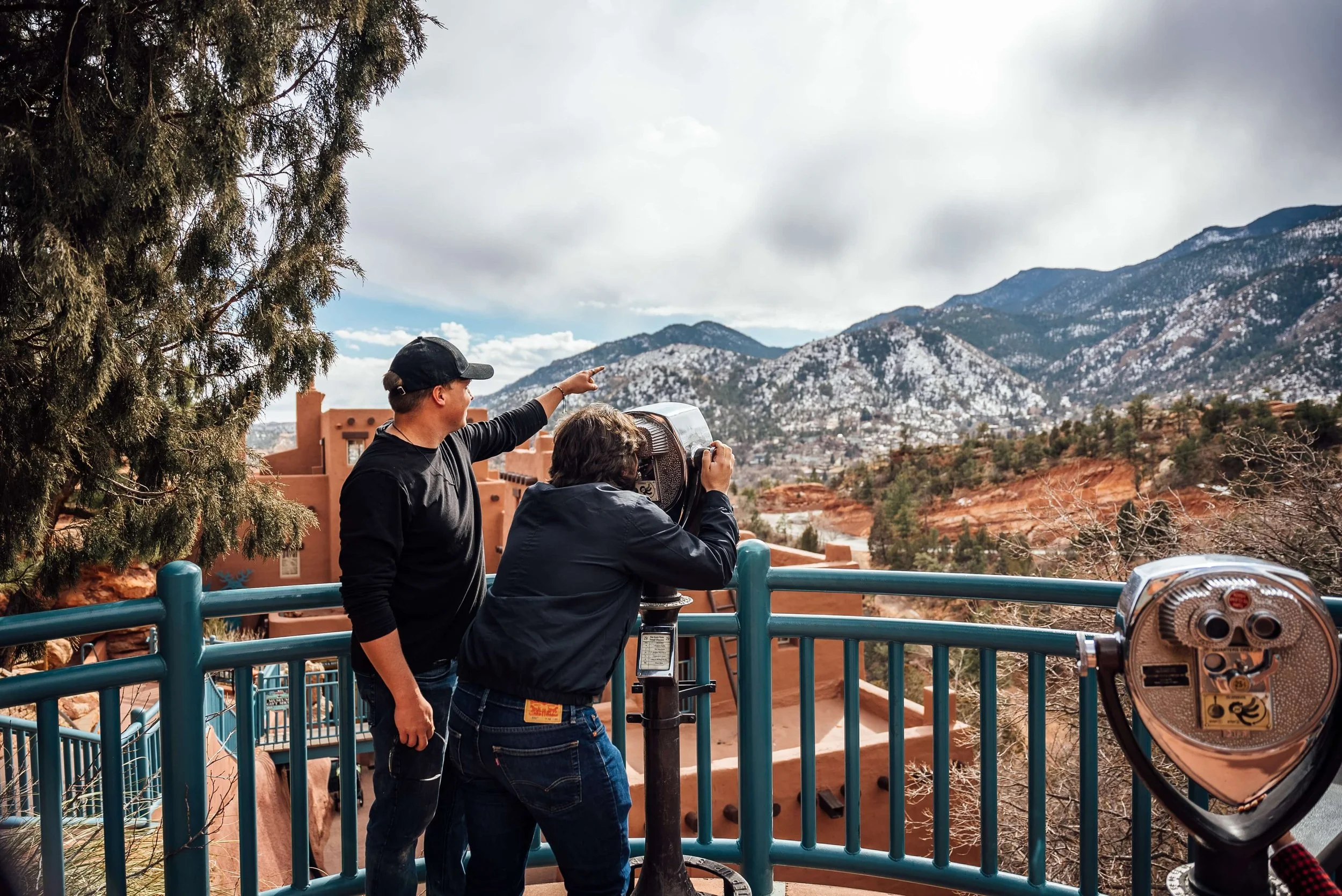 Two people looking through a coin-operated telescope at the Manitou Cliff Dwellings in Manitou Springs, Colorado.