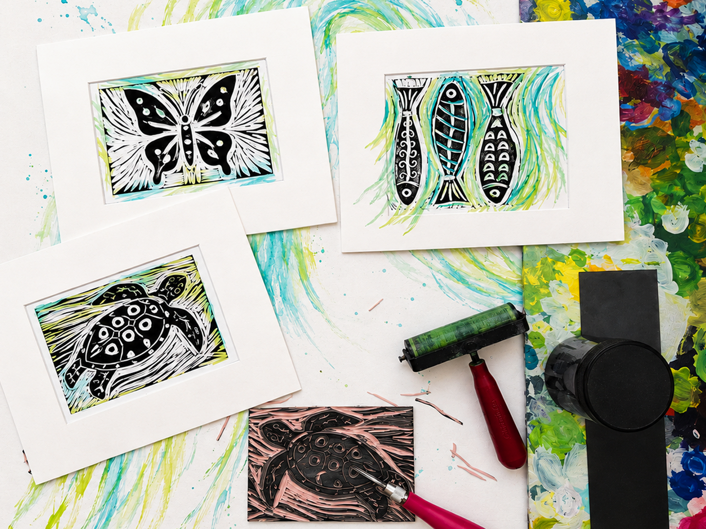 Art supplies and prints of black and white paintings of animals, including a butterfly, fish, and turtle, on a colorful artist's workspace.