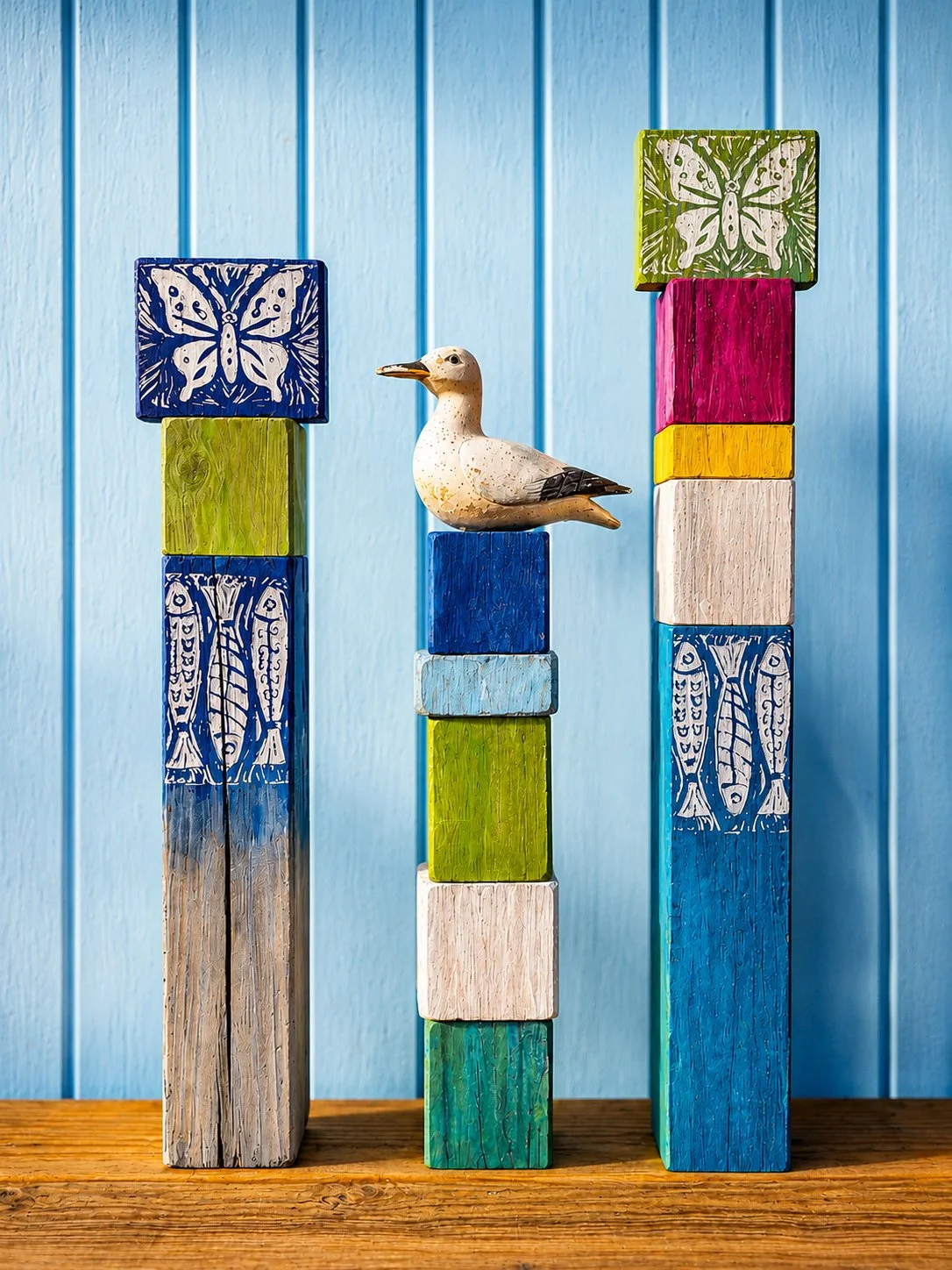 Colorful decorated wooden blocks stacked in two towers with a ceramic bird figurine in between, set against a blue paneled wall.