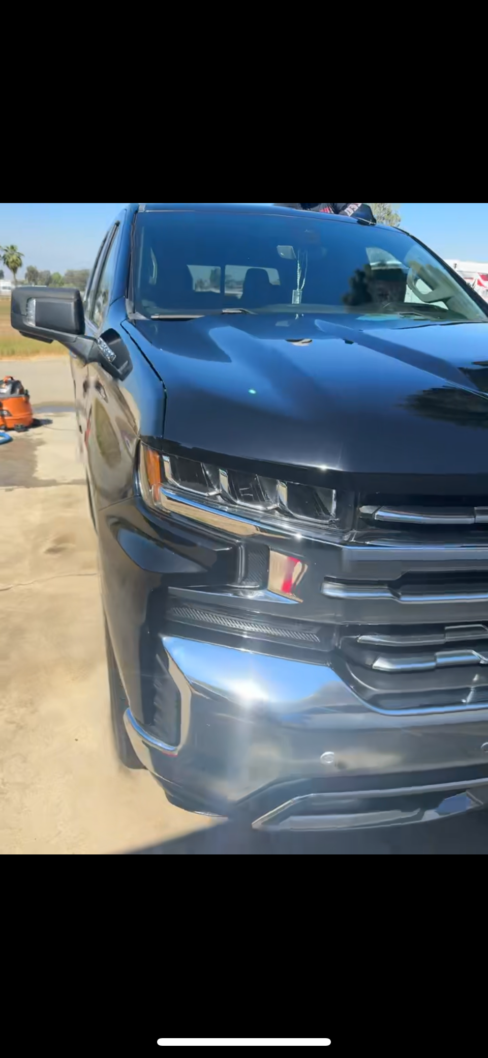 Black pickup truck parked on concrete surface with tools and equipment nearby, clear sky in the background.