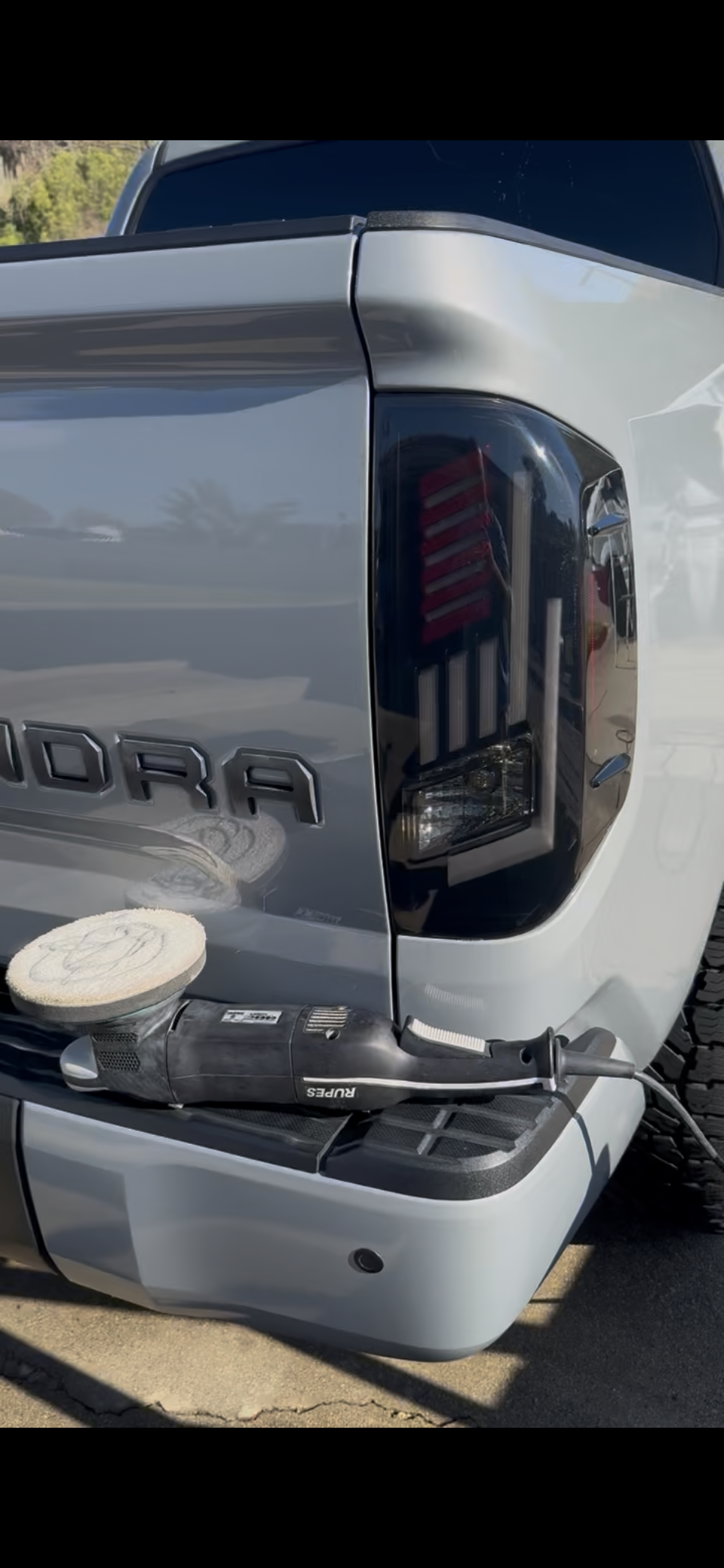 Close-up of the rear of a silver Toyota Tundra pickup truck with a black taillight and a polishing tool resting on the bumper.