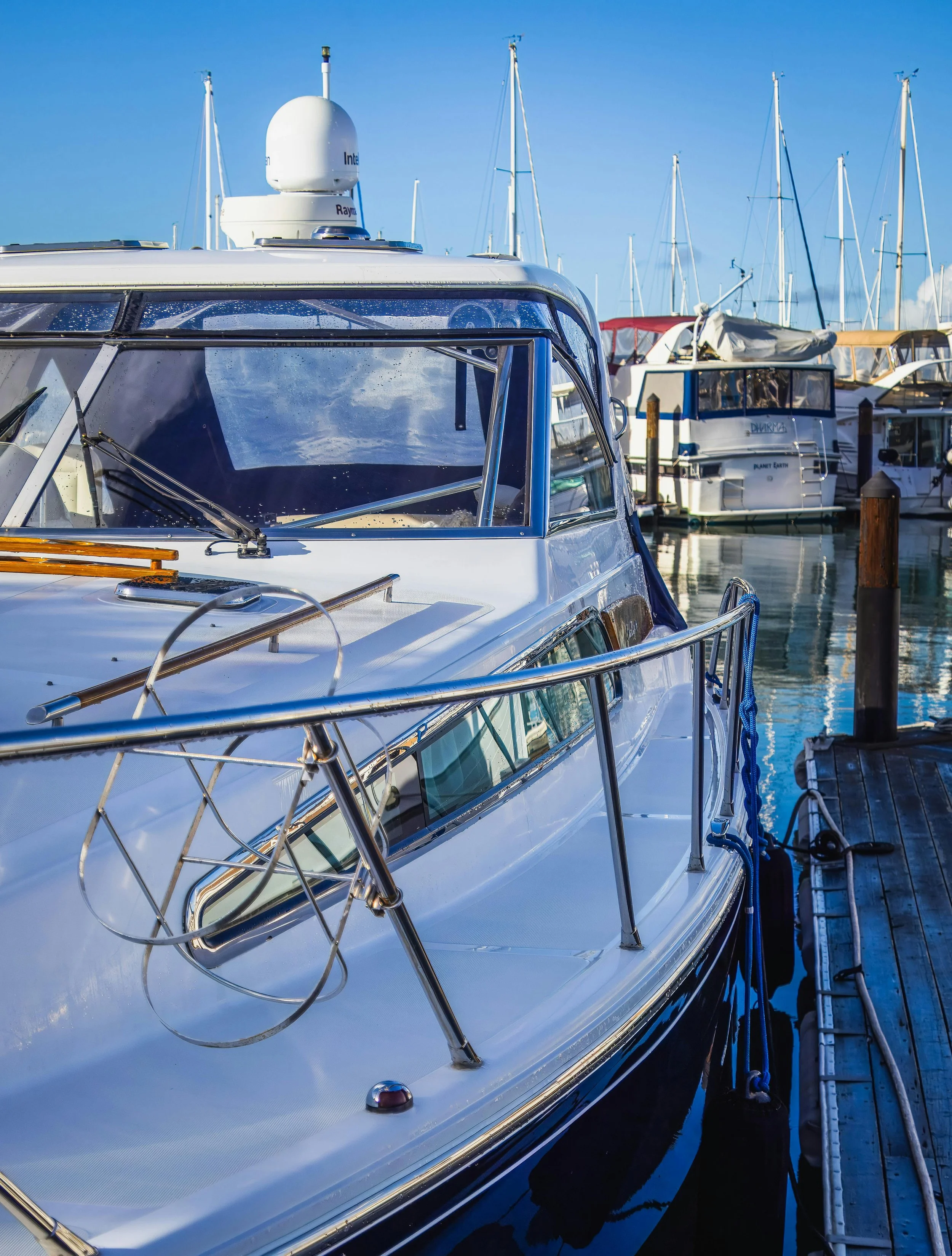 View of a marina with motorboats and sailboats docked, clear blue sky, presence of radar on the boat in the foreground, water reflecting the boats. Salt protection