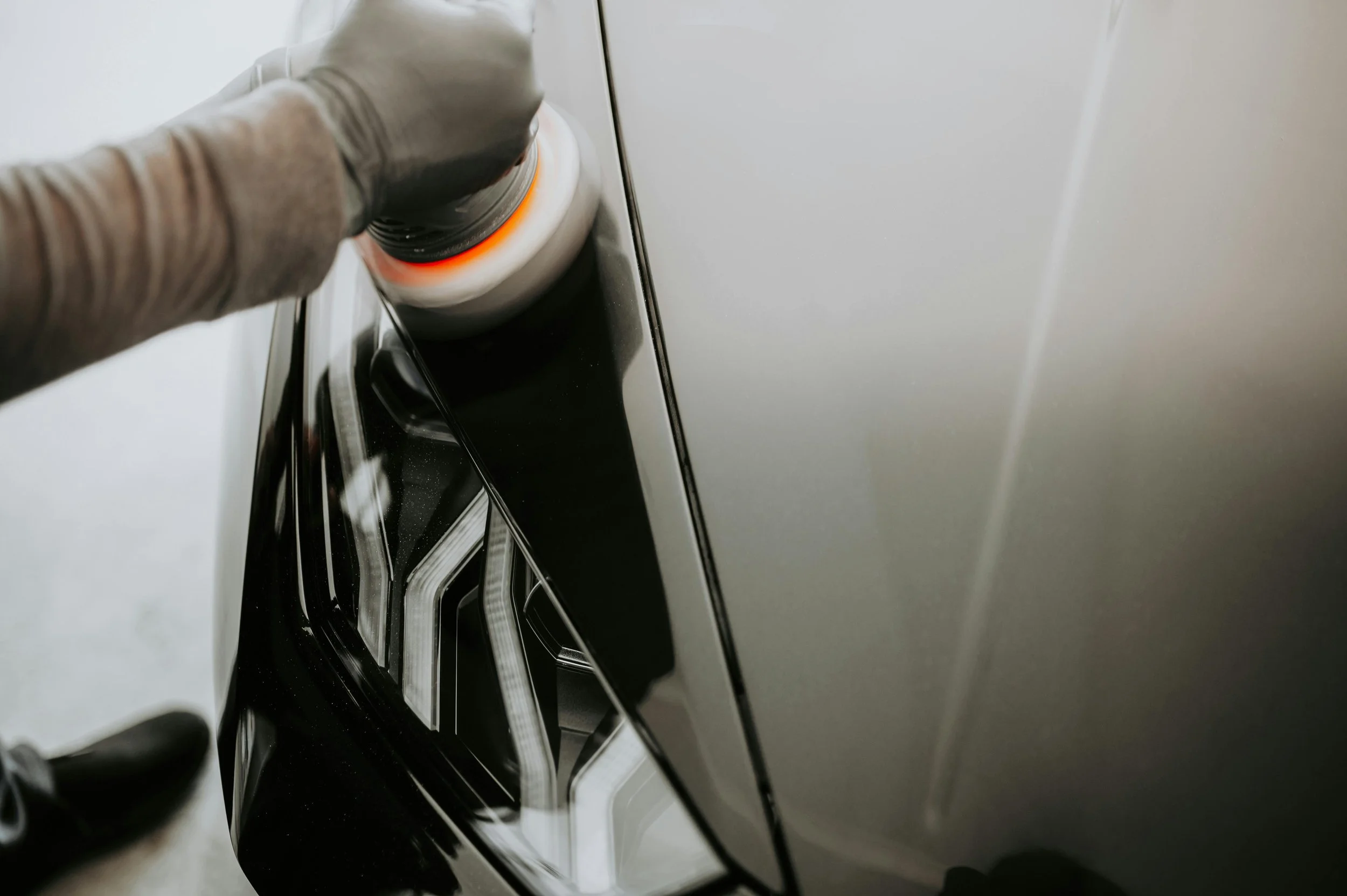 Person wearing gloves cleaning the side of a white vehicle with a handheld cleaning tool.