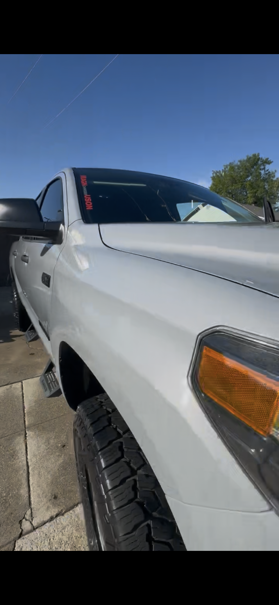 White pickup truck parked on concrete surface under clear blue sky with trees in the background.