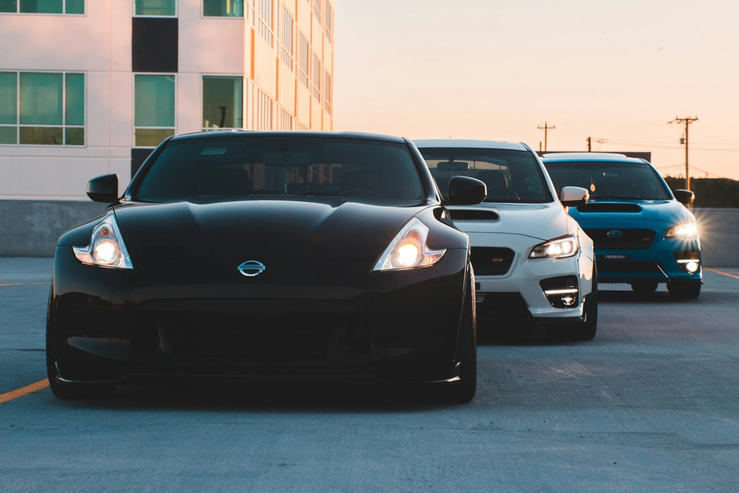 Three cars parked in a parking lot during sunset with a building and power lines in the background.