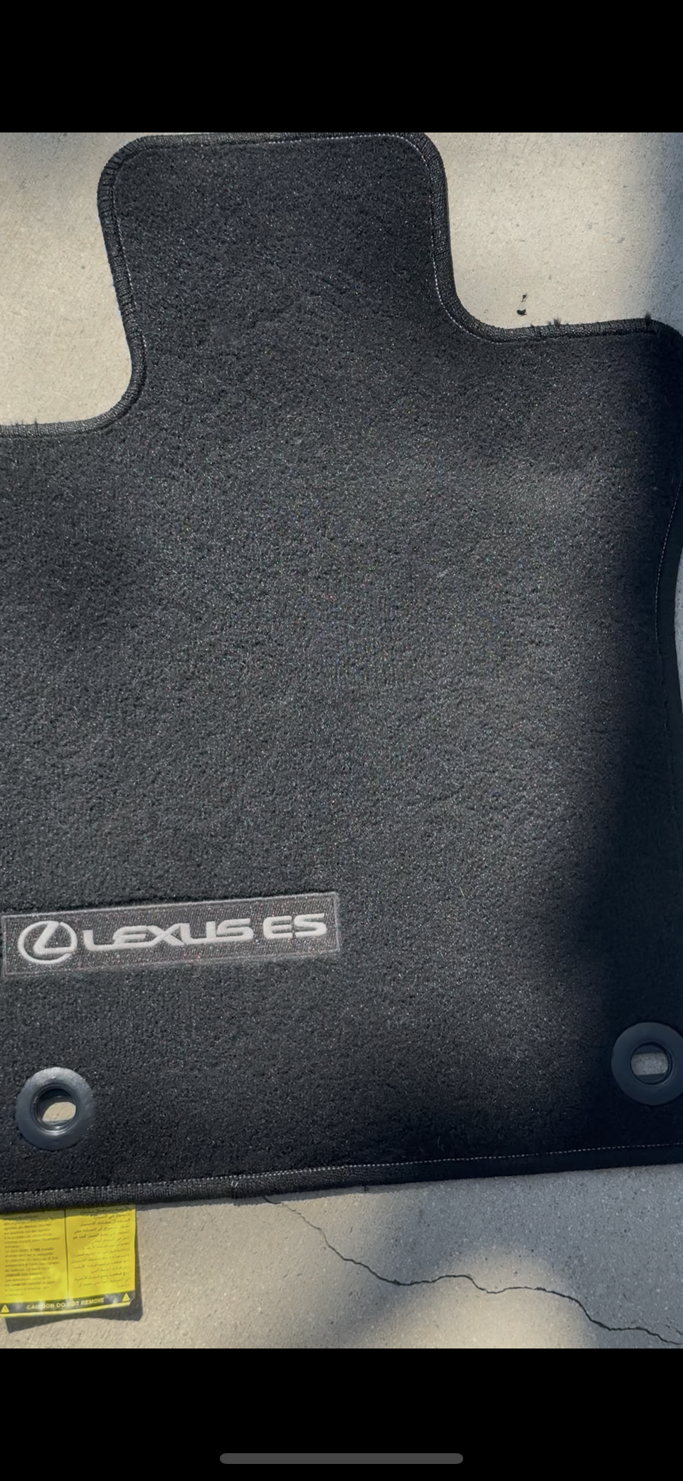 Black Lexus ES car floor mat with the Lexus logo, placed on a gray concrete surface.