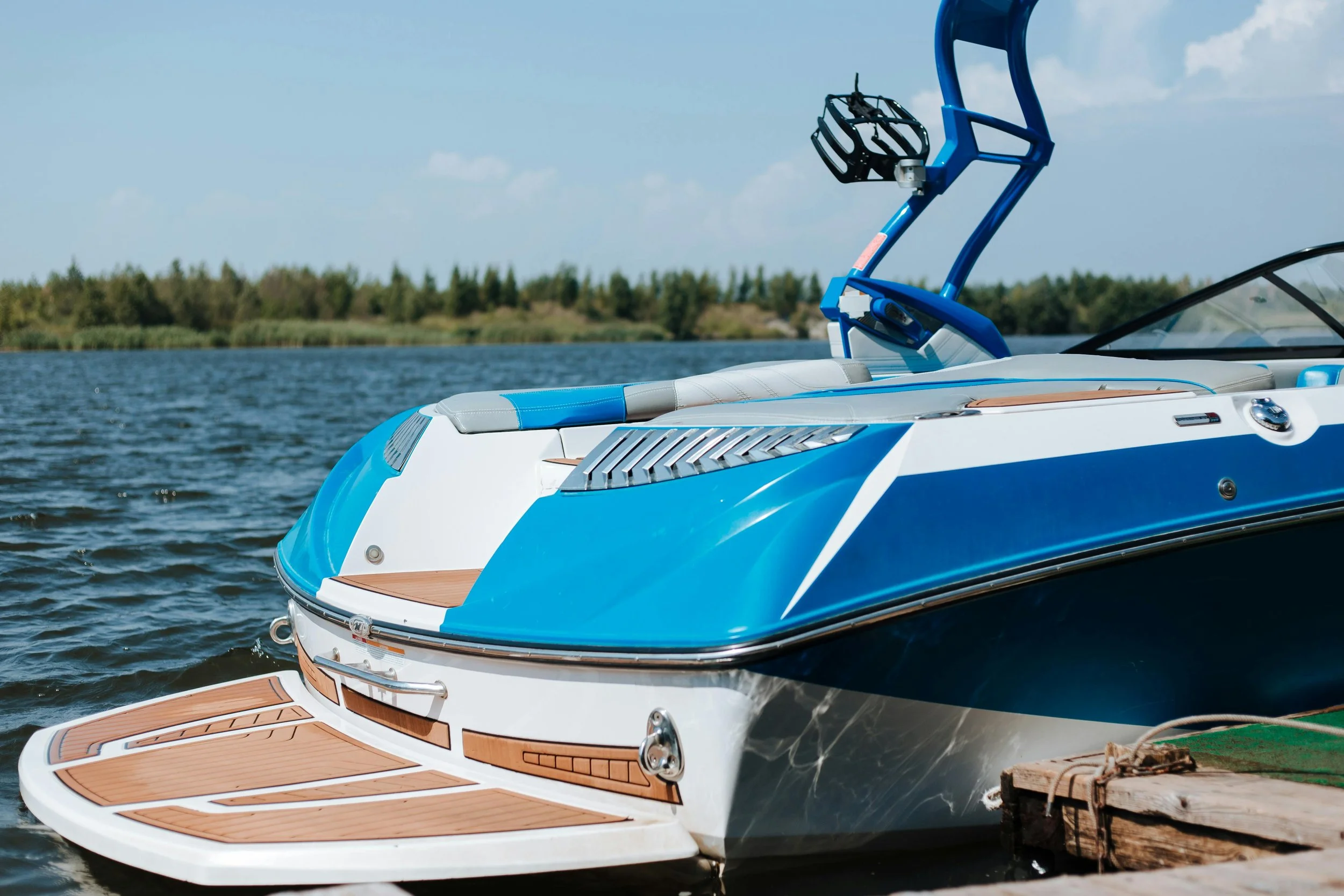 A blue and white motorboat docked at a wooden pier on a lake with a treeline in the background under a partly cloudy sky. Gel Restoration