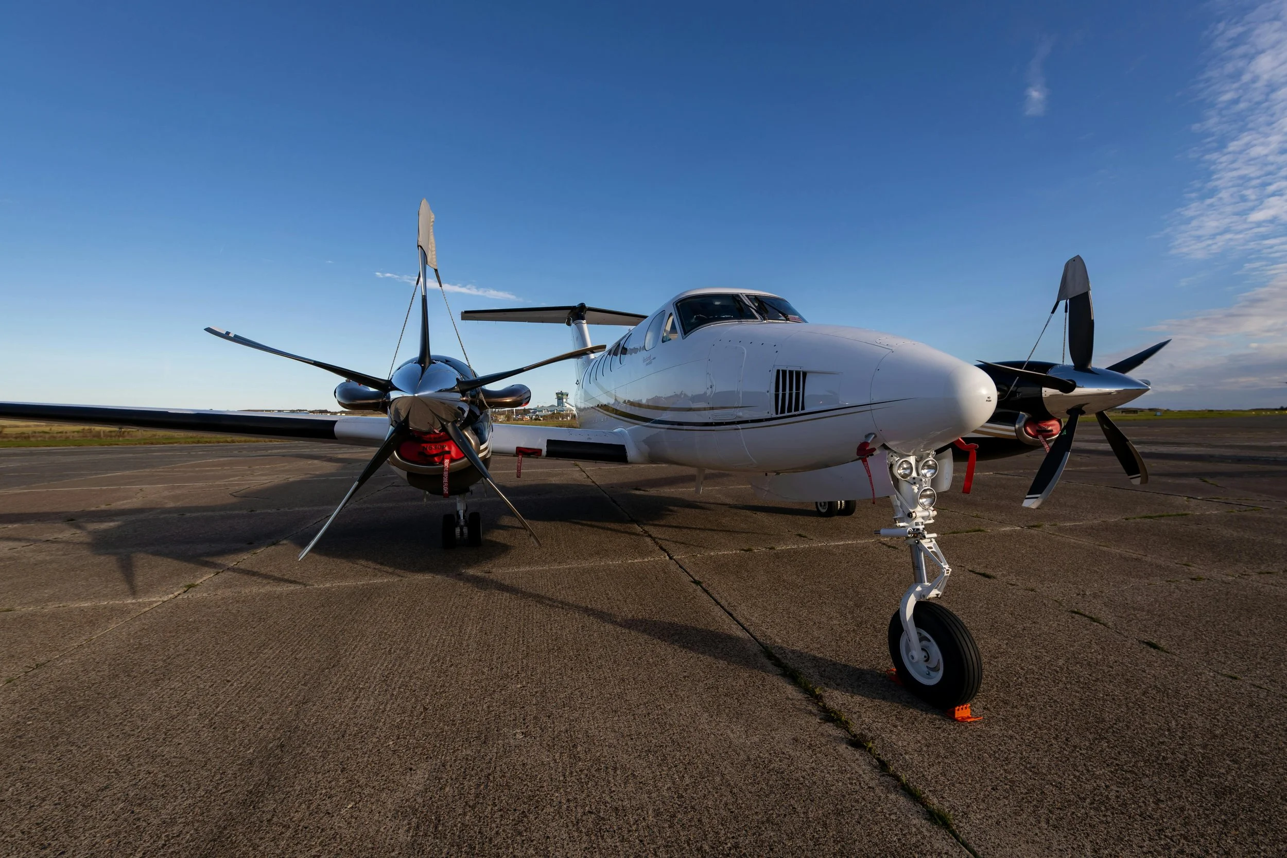A futuristic white aircraft with twin propellers parked on an airstrip under a blue sky with some scattered clouds.