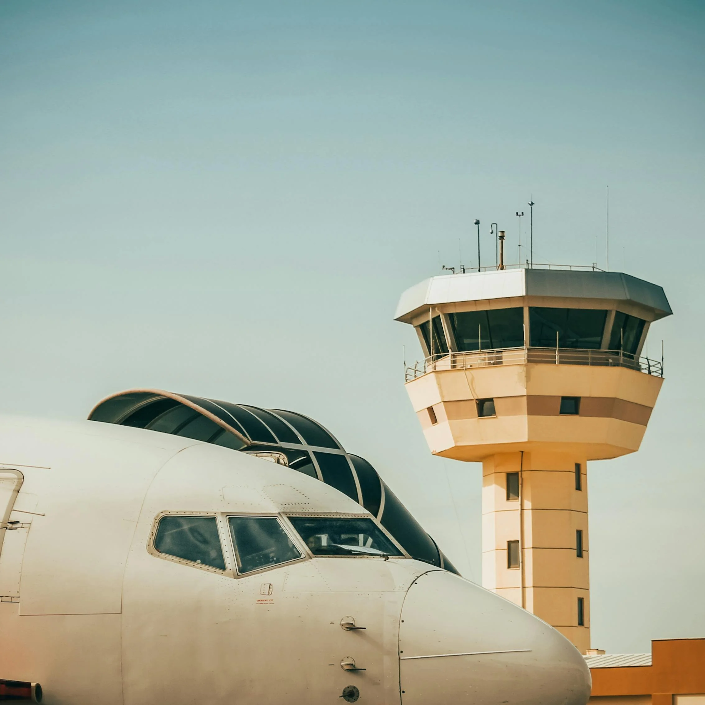 Side view of an airplane parked at the airport with a control tower in the background against a clear sky.
