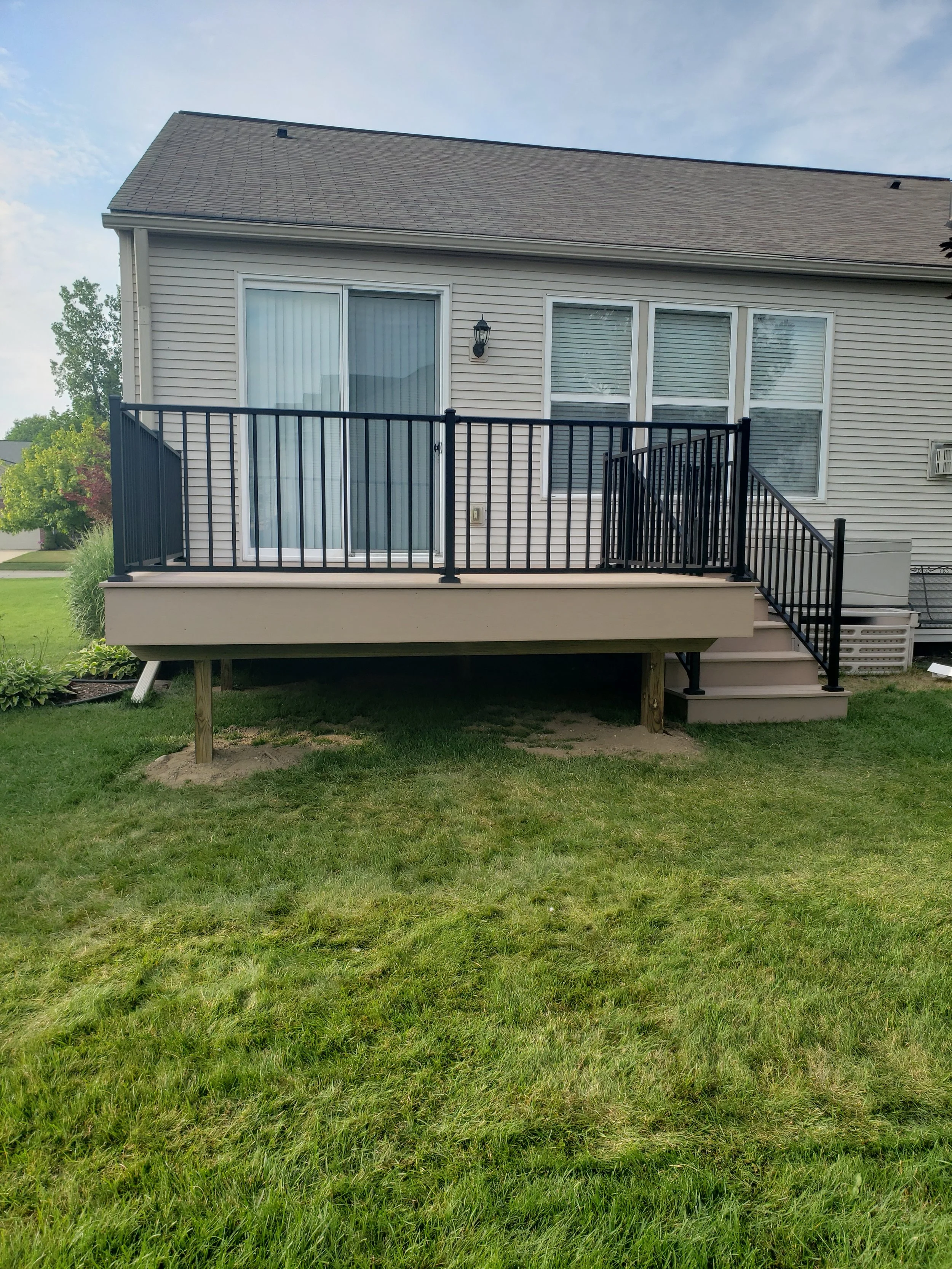 Backyard deck with black railing, stairs, sliding glass door, and a house exterior with windows and siding.