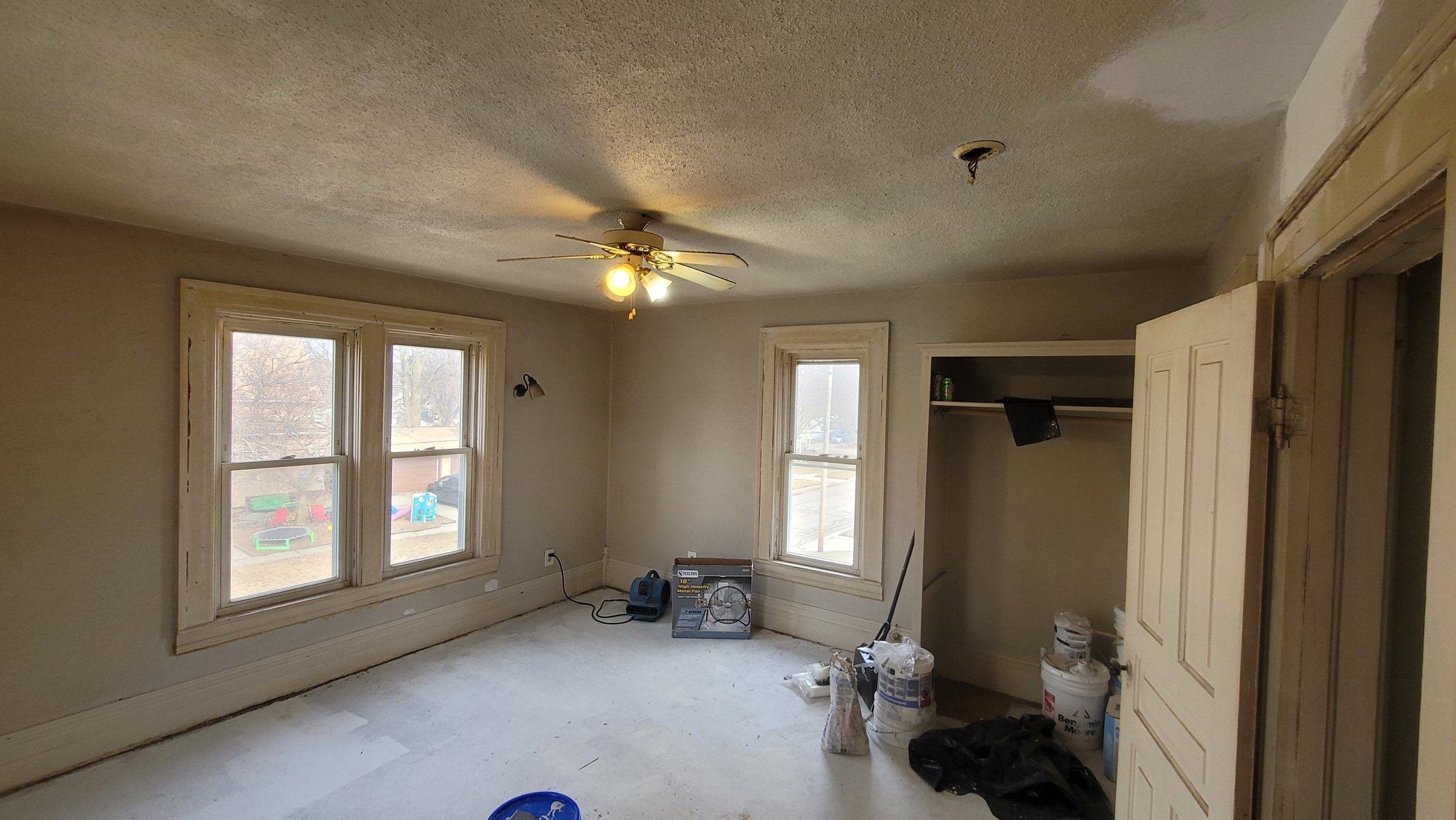Room under renovation with new windows, a ceiling fan, and construction supplies on the floor.