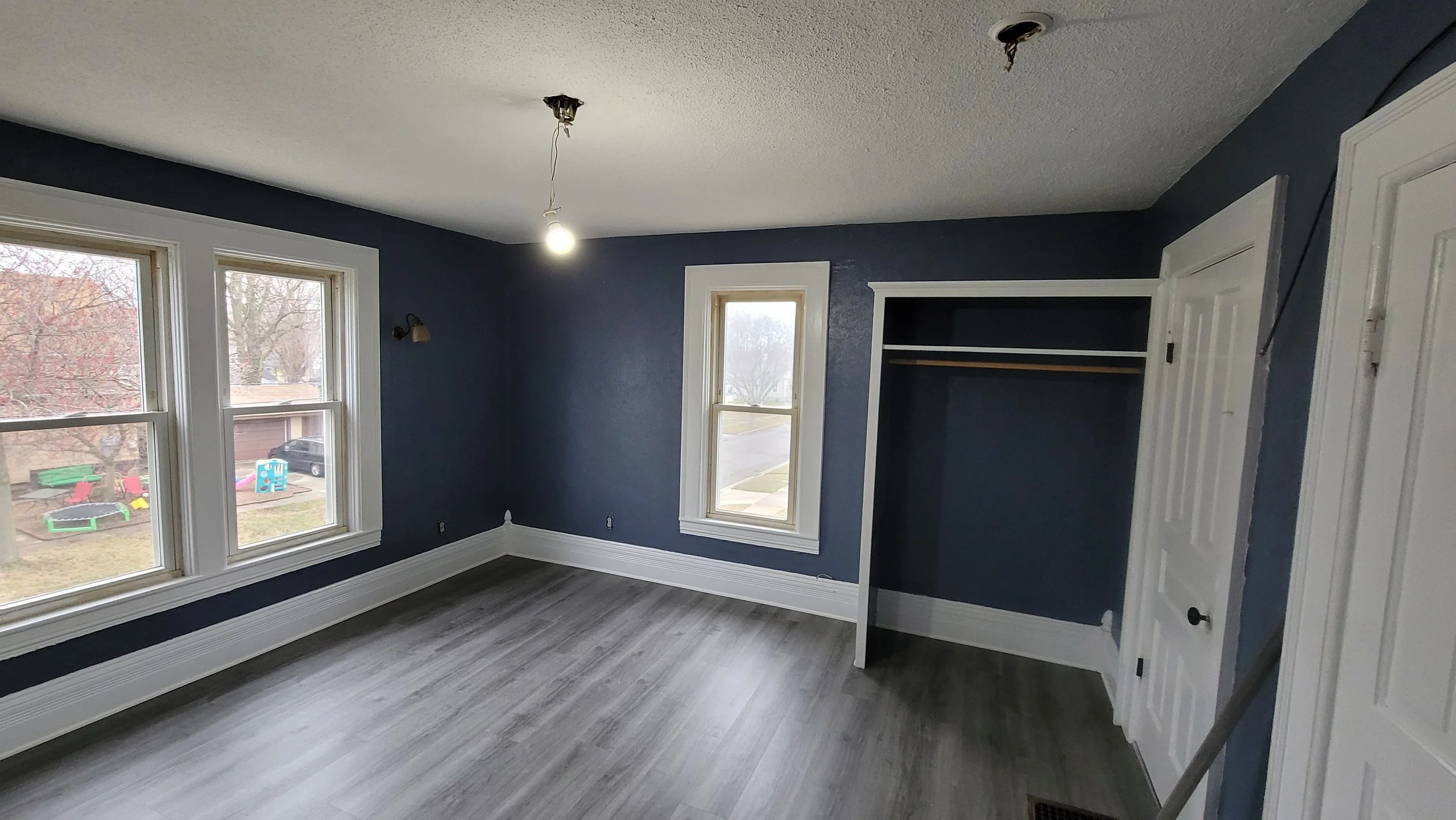 Empty room with blue walls, large windows, a closet, and gray wood flooring.