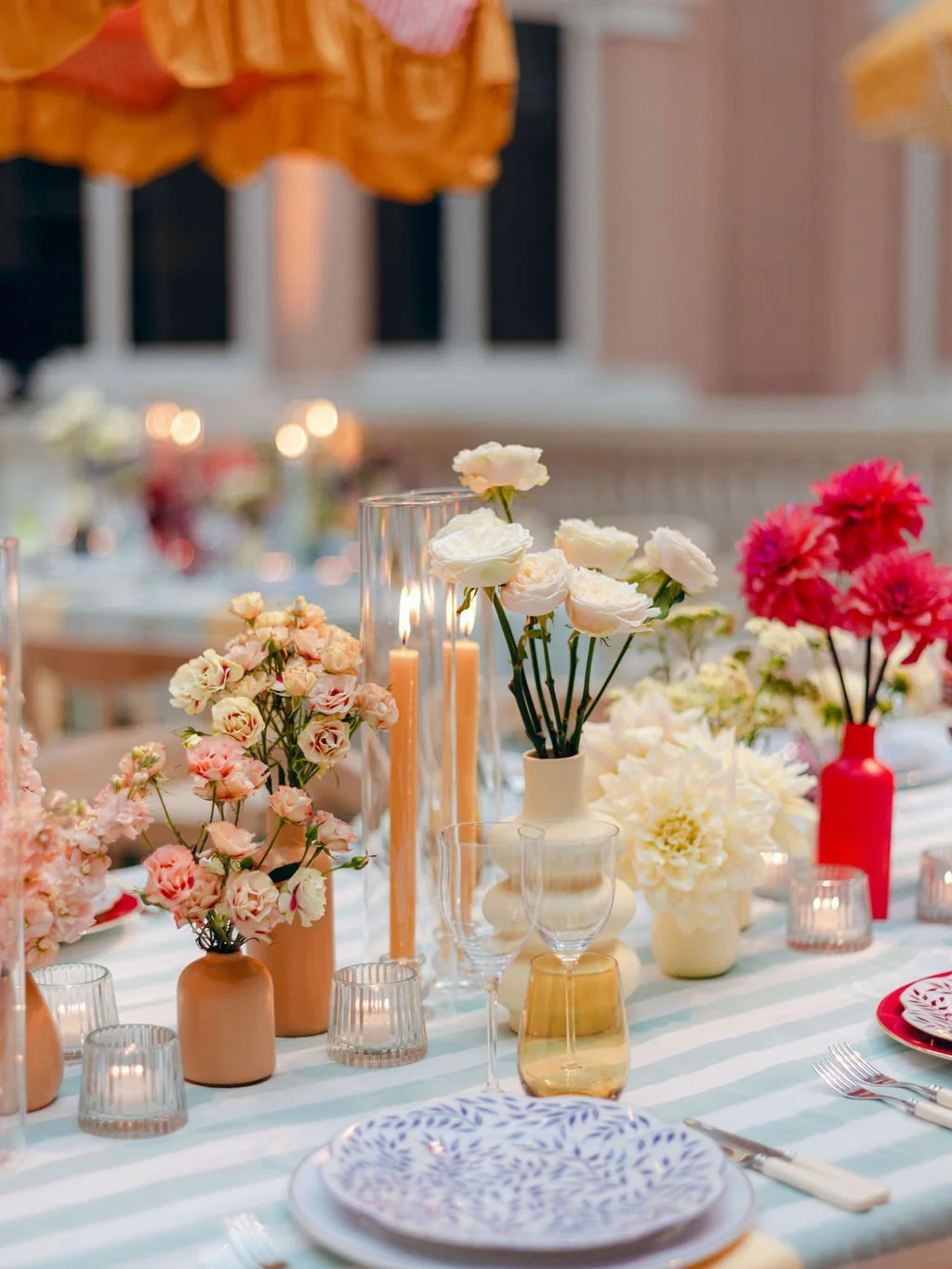 A table decorated with colorful flowers in vases, candles, and plates set for a meal, in a decorated indoor space.