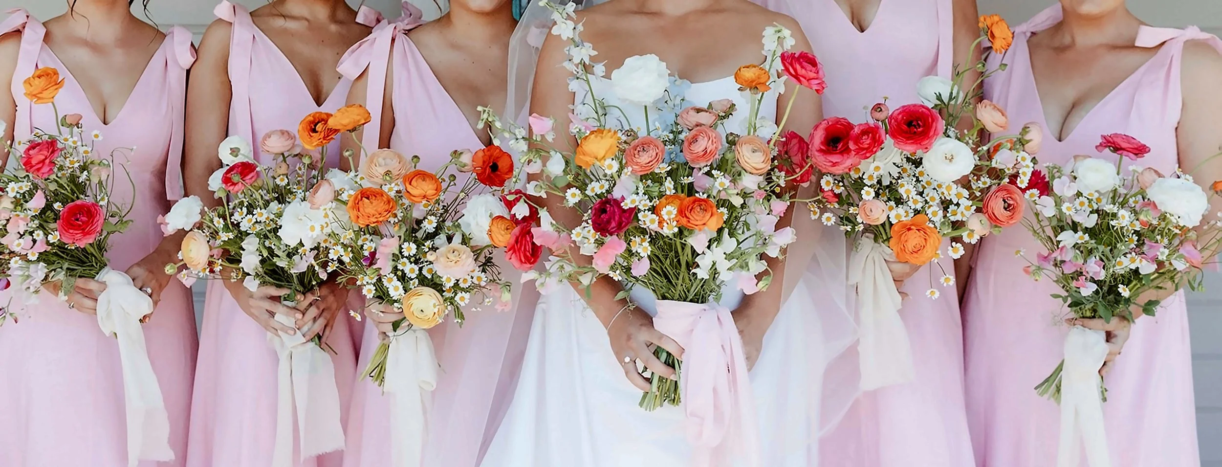 Group of women in pink dresses holding colorful flower bouquets at a wedding.