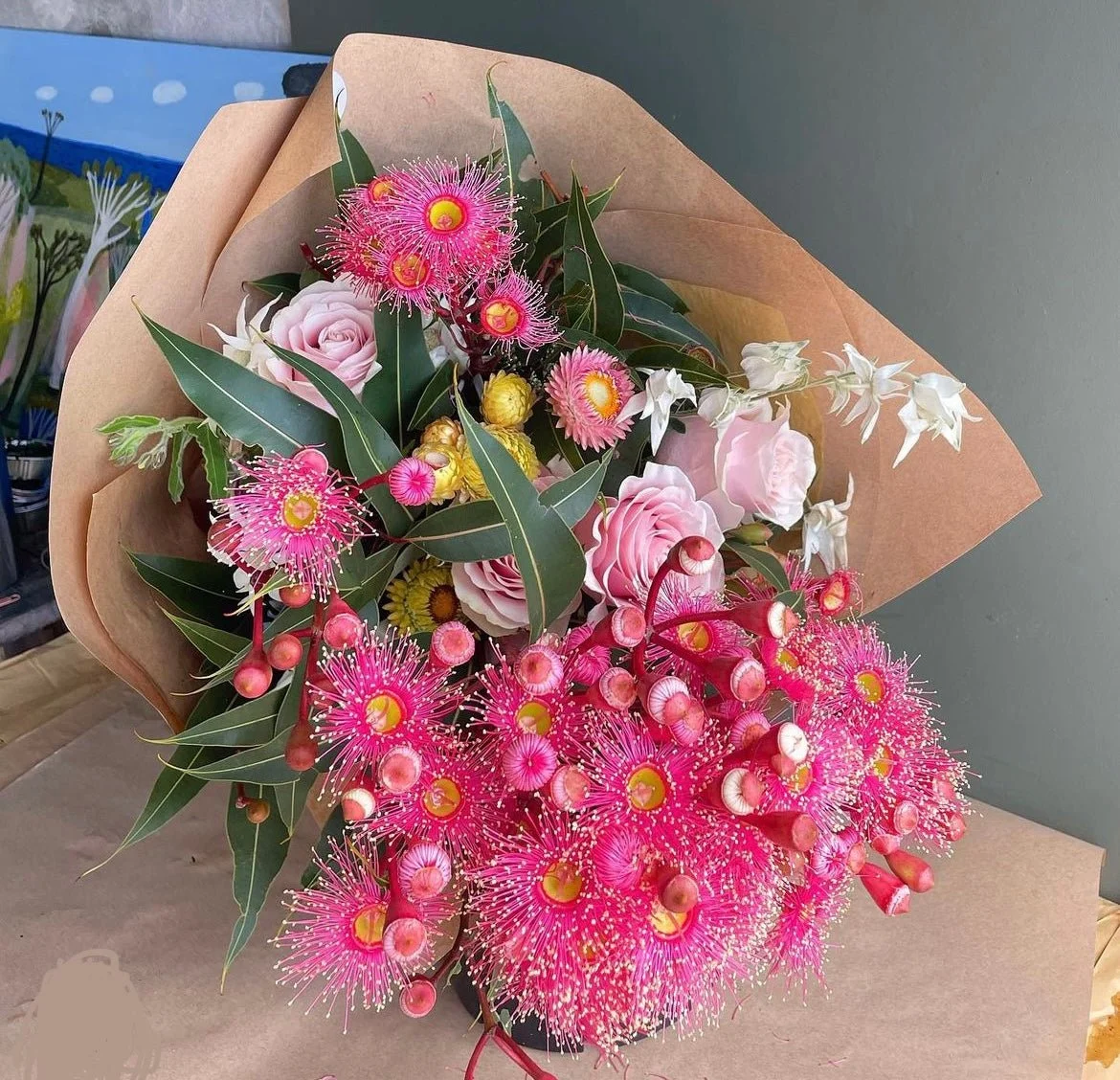 A bouquet of pink, white, and yellow flowers wrapped in brown paper with green leaves.