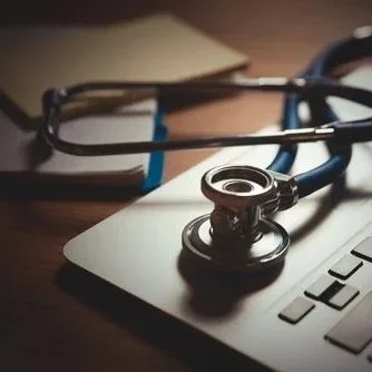 Stethoscope on a closed laptop, with a notebook and eyeglasses nearby.