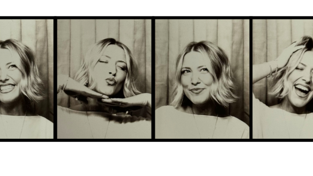 Four black-and-white photos of a woman with shoulder-length wavy hair in a photo booth, showing different playful expressions and poses against a wooden background.