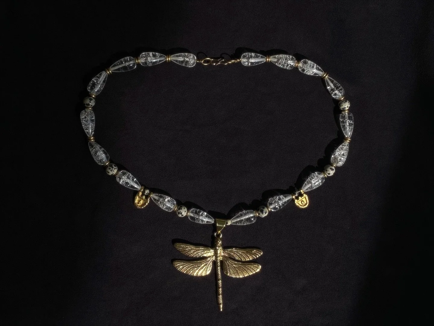 a relic of light and shadow

Brass dragonfly. Clear quartz beads. Dalmatian jasper details. 
One-of-a kind. Unisex.
