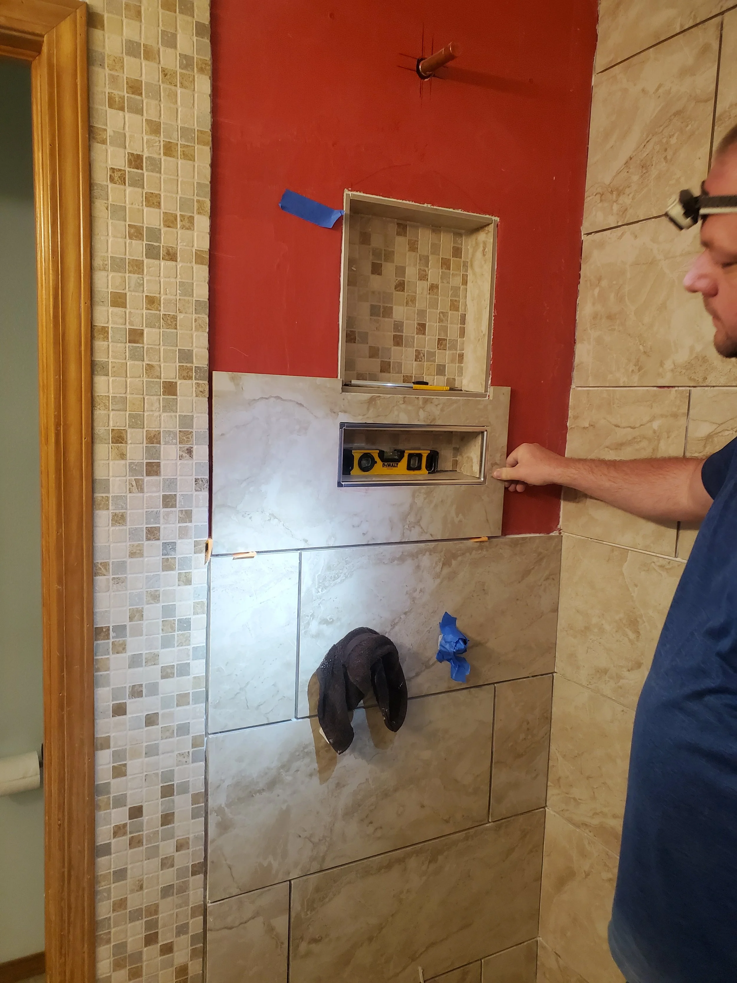 A person installing tile around a recessed wall niche in a bathroom, with a level tool placed inside the niche and a towel hanging on the wall.