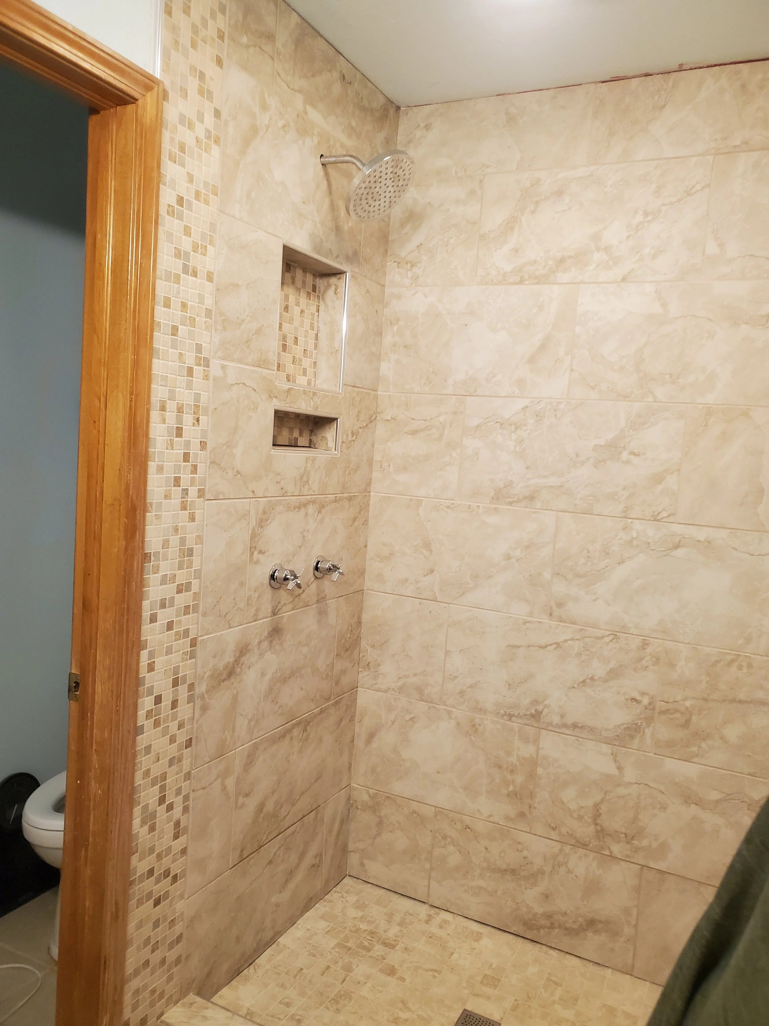 A shower area with beige marble tiles on the walls and floor, featuring a built-in wall niche, a showerhead, and two knobs for water control.  Colorado Springs