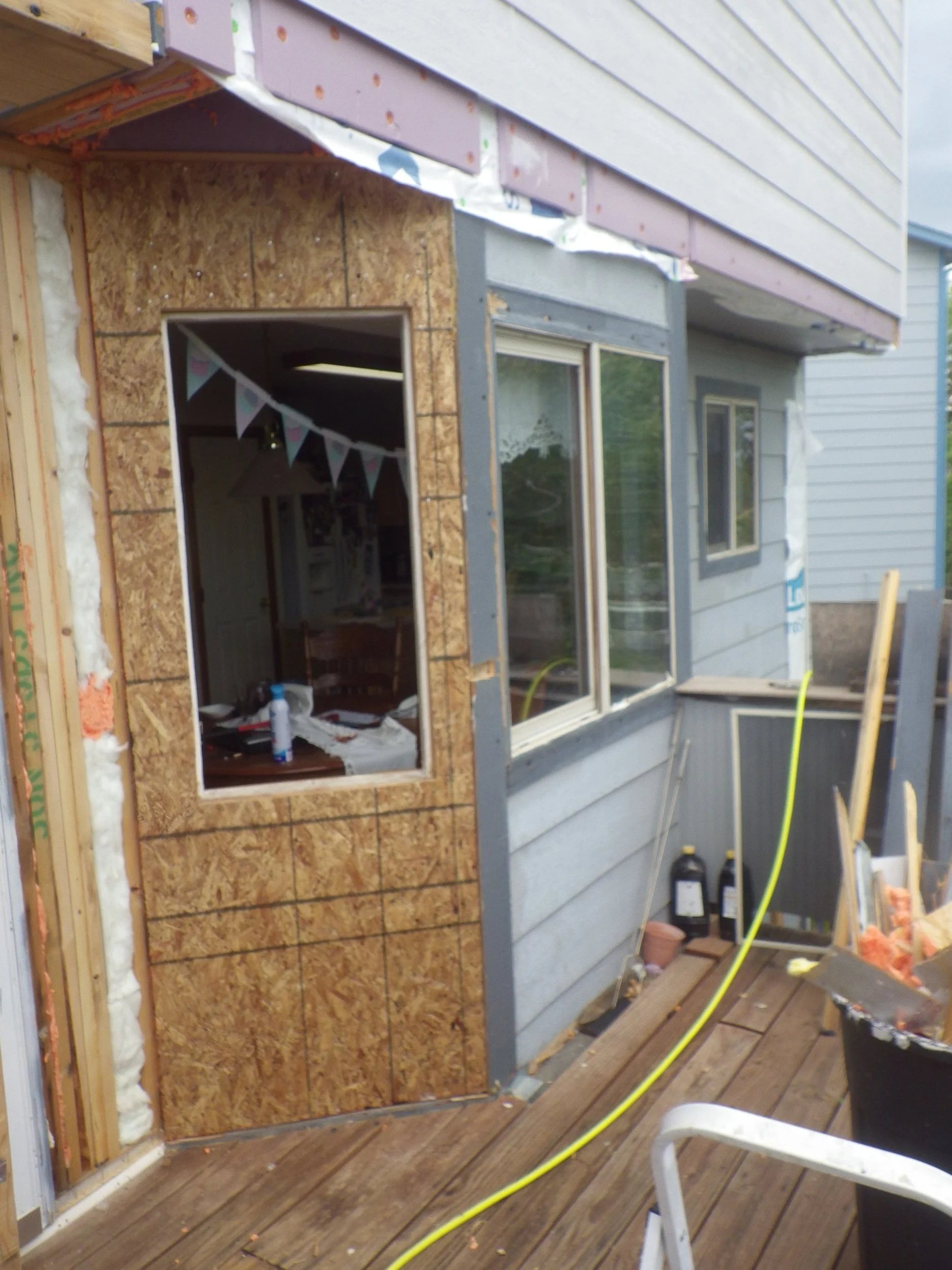 Construction site of a house with unfinished walls, wooden framing, and siding, with tools and construction materials outside.