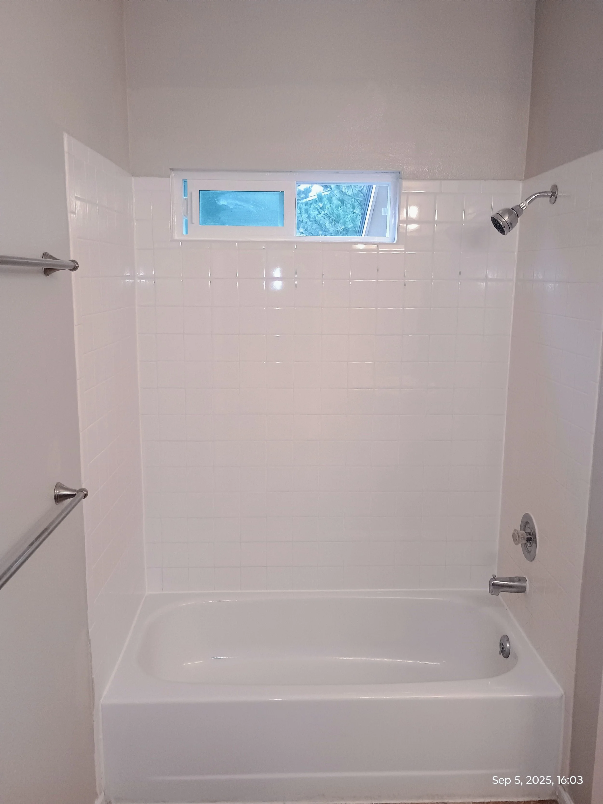Empty white bathtub in a bathroom with white tiled walls and a small window. There are bath fixtures including a showerhead, a tub faucet, and a volume control. The photo is taken from the perspective of standing in the bathroom. The date and time shown on the bottom right corner is September 5, 2025, at 4:03 PM.