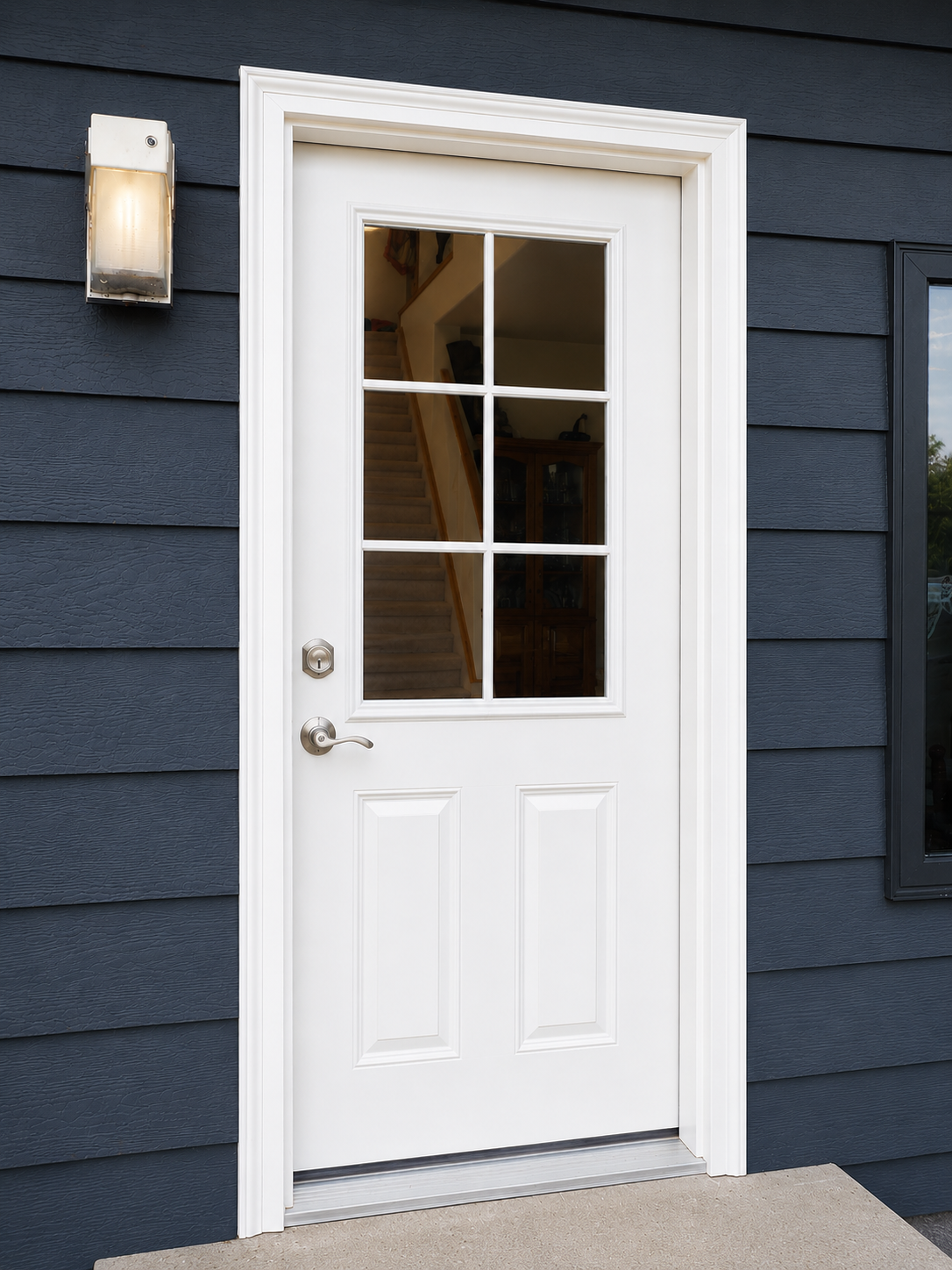 Exterior view of a white glass-paneled door with a silver handle, set in a dark blue house with horizontal siding, next to a wall-mounted outdoor light fixture.