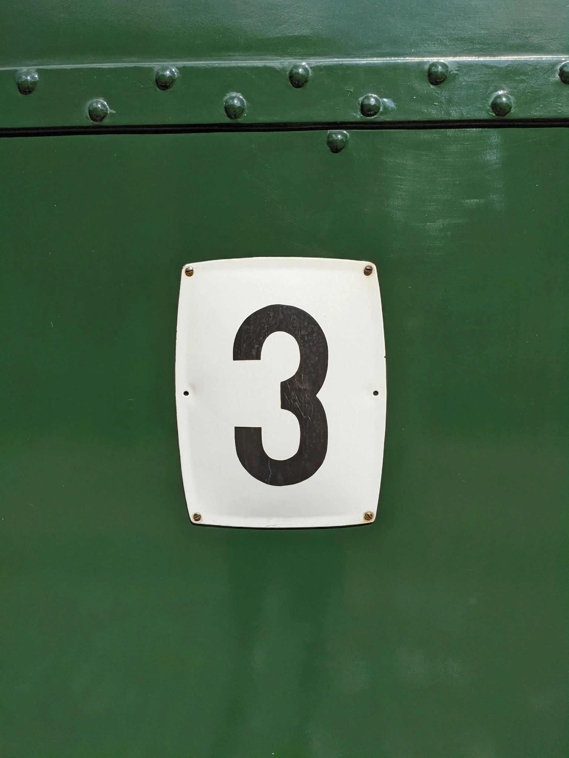 Close-up of a white plate with the number 3 on a green surface.
