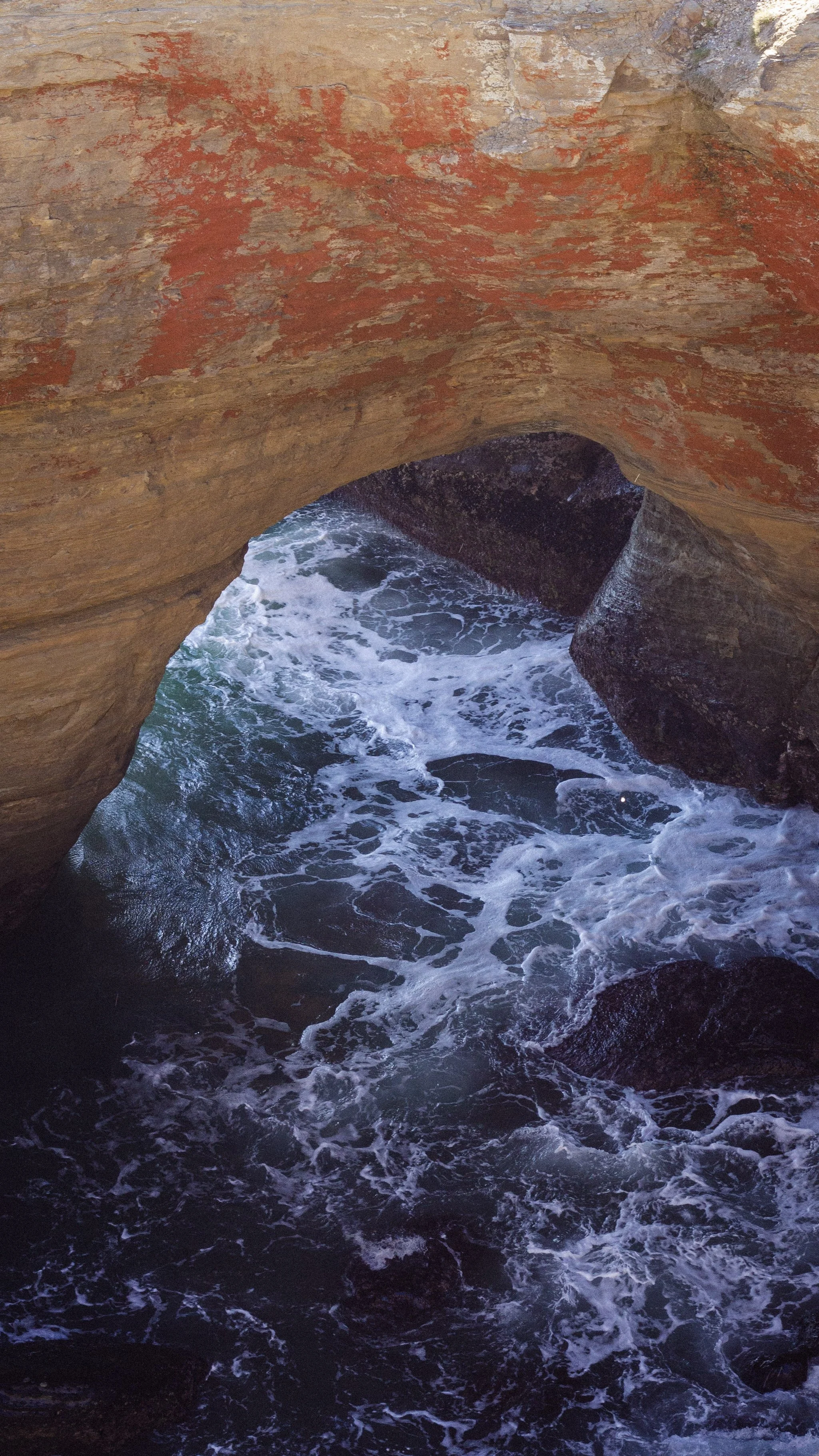 Rock formations with a natural ocean arch over turbulent water and waves crashing against rocks underneath.