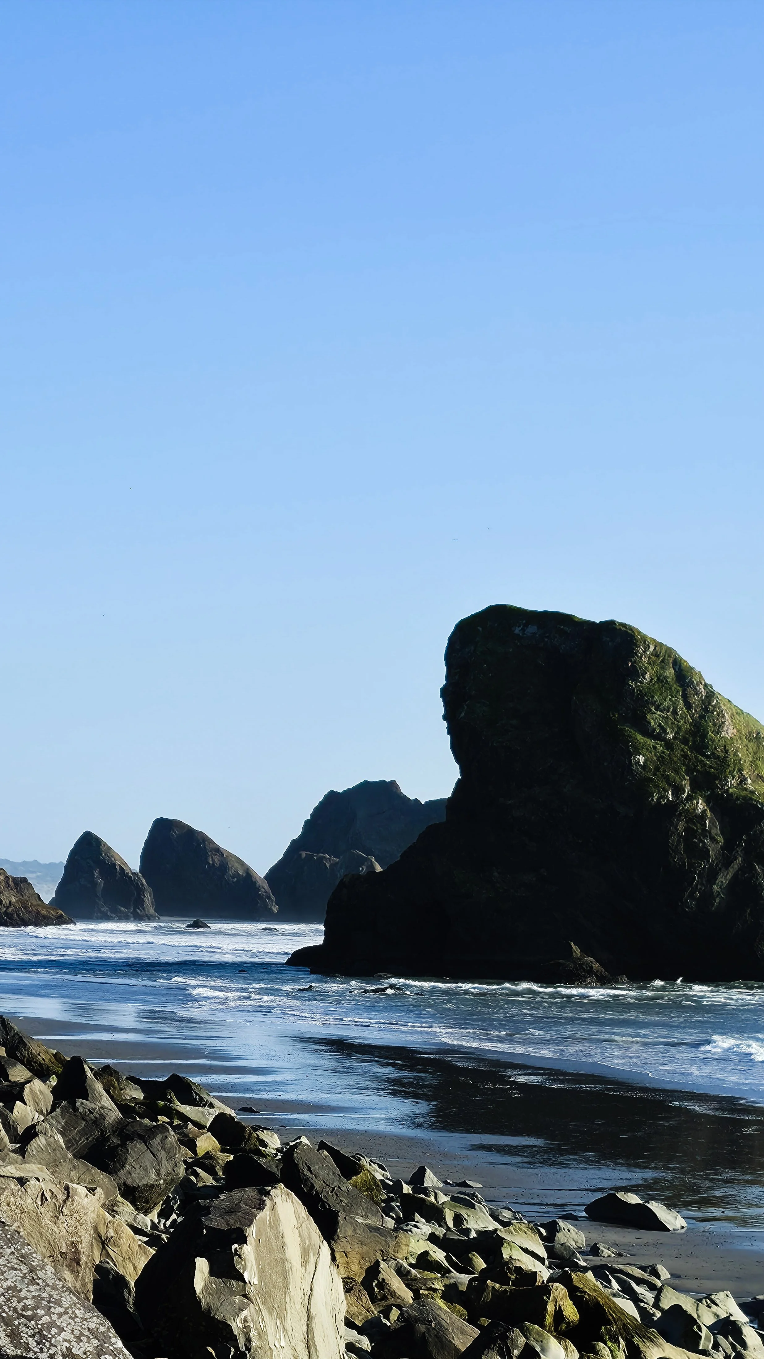 Large rocks and boulders along a shoreline with tall rocks in the background and blue sky above.