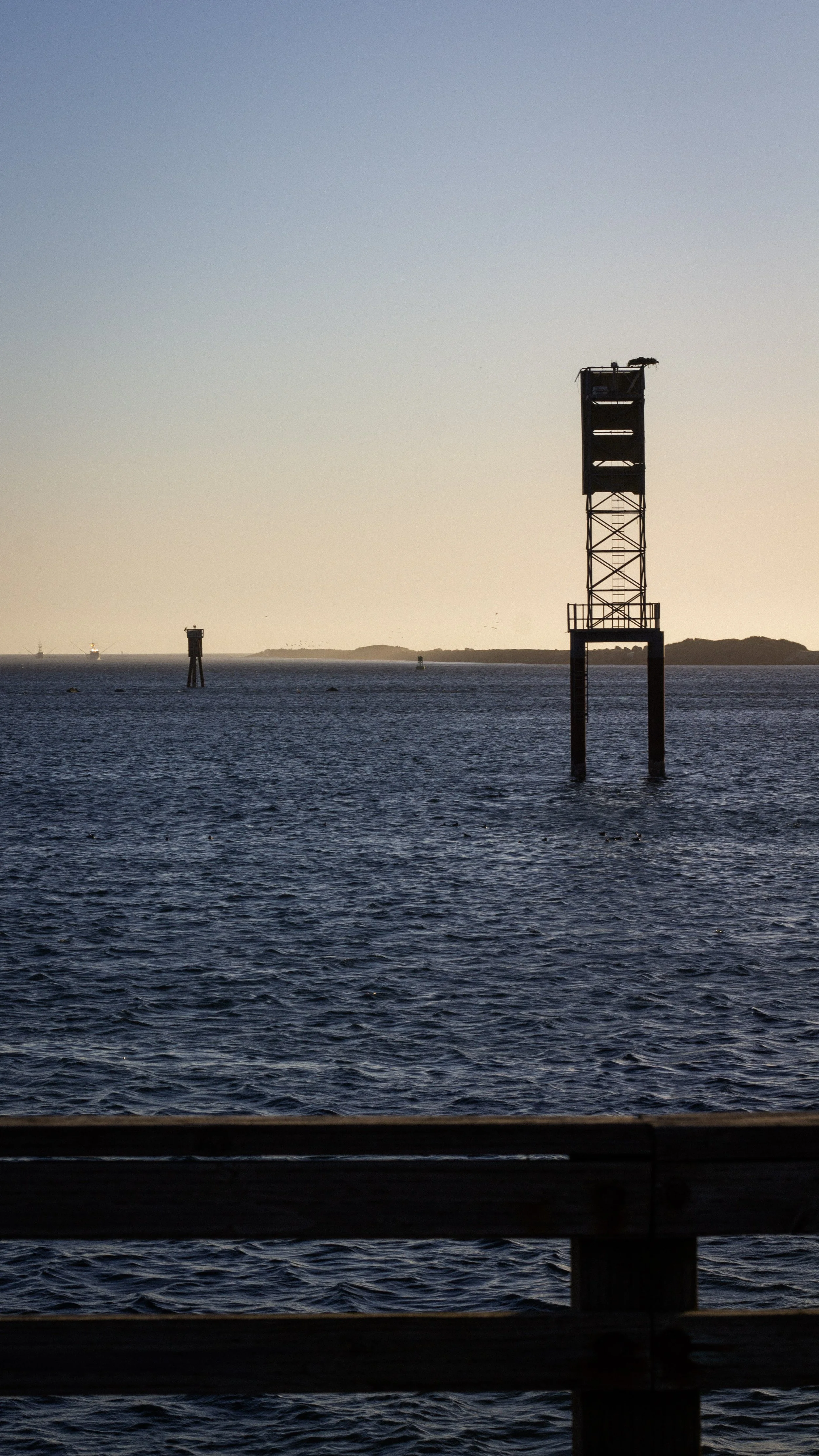 View of the ocean with navigational buoys and island in the distance during sunset.