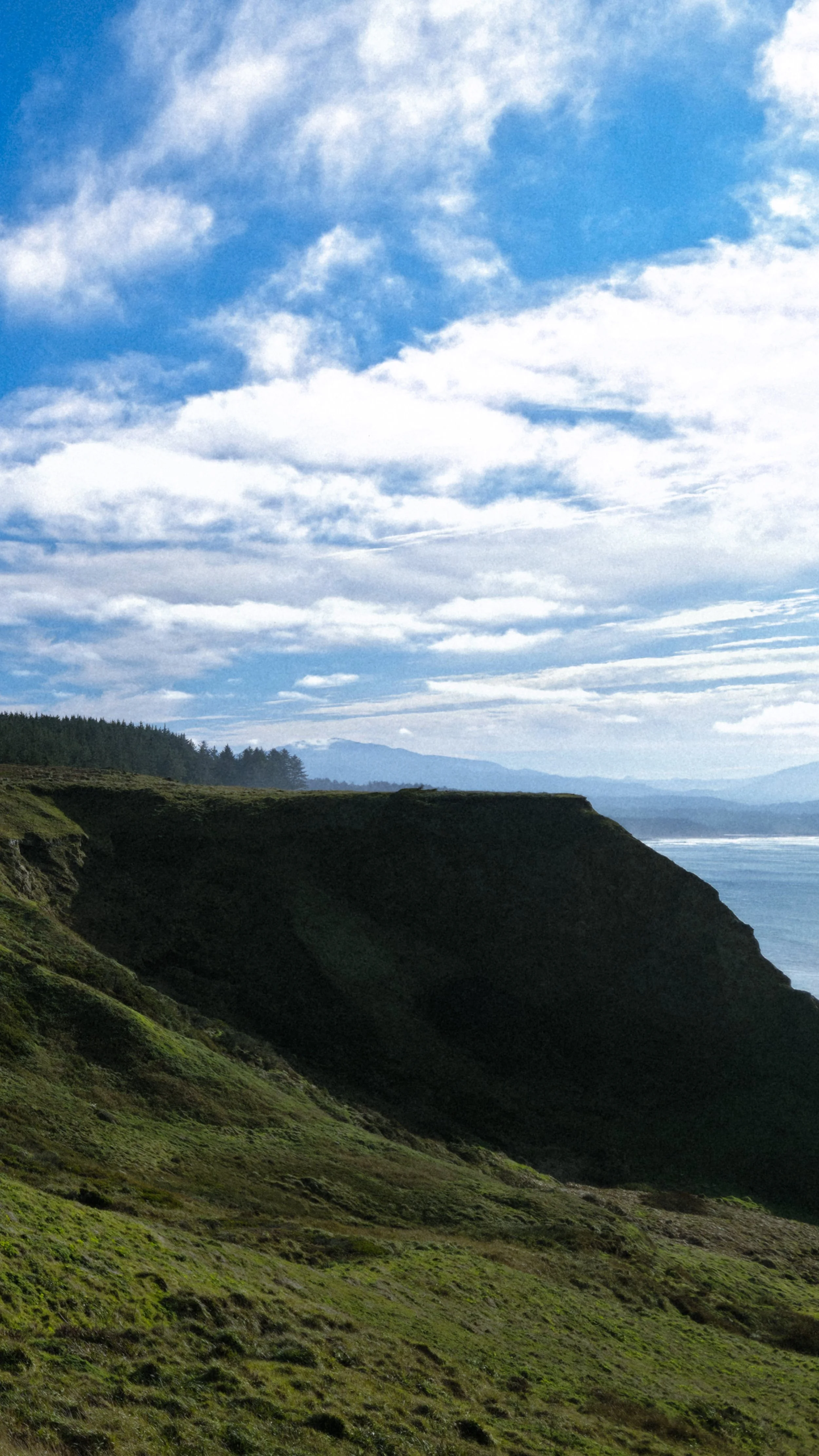 Coastal landscape with green cliffs, ocean, and cloudy blue sky.