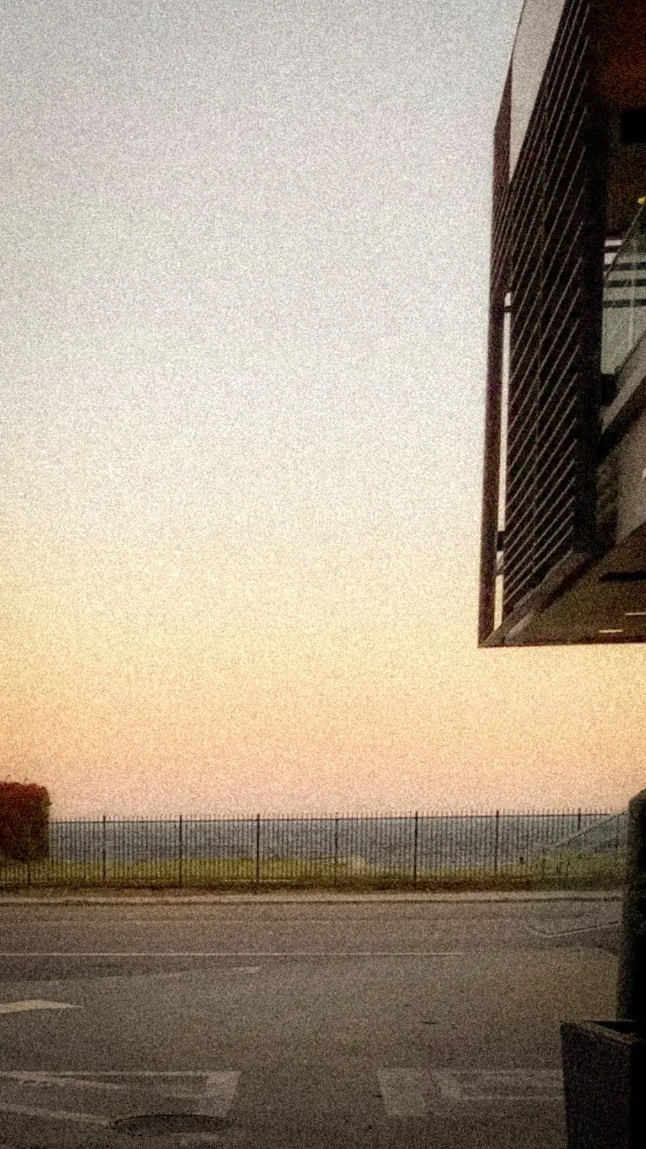 A view of a sunset or sunrise sky over a fenced field, with part of a building visible on the right side of the image.