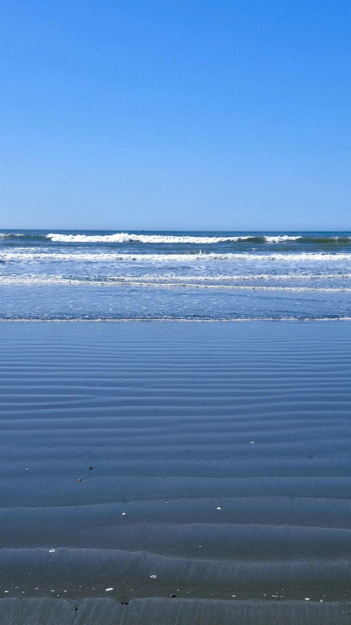 Calm ocean waves gently hitting a sandy beach on a clear day with blue sky.