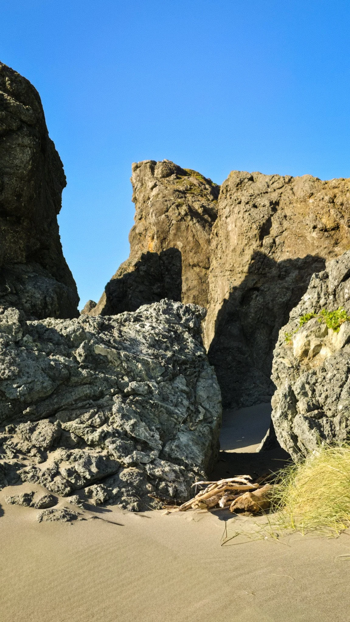 Large rocks and boulders on a sandy beach with tall cliffs in the background and a clear blue sky.