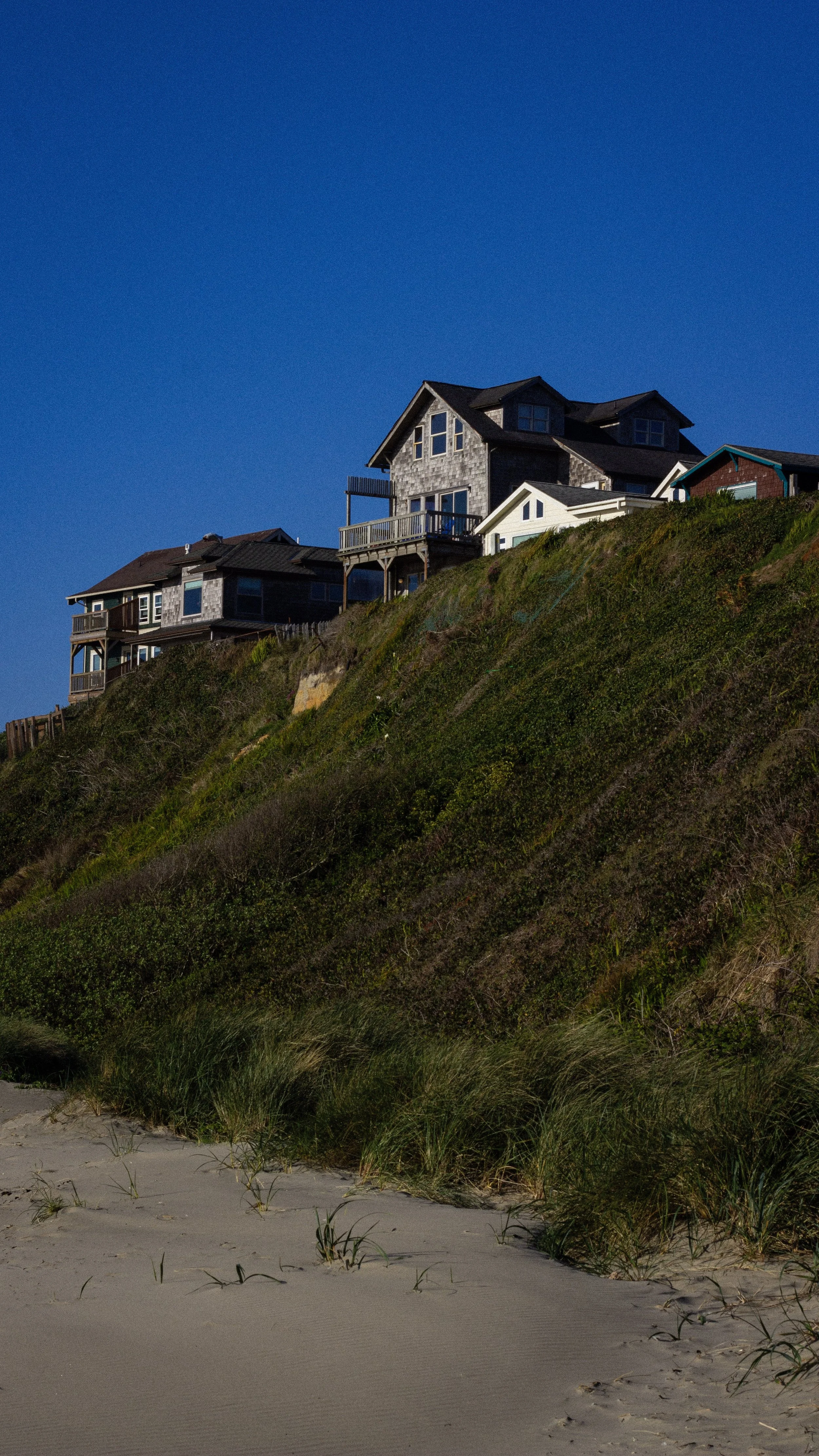 Houses perched on a grassy, sandy hillside against a clear blue sky.