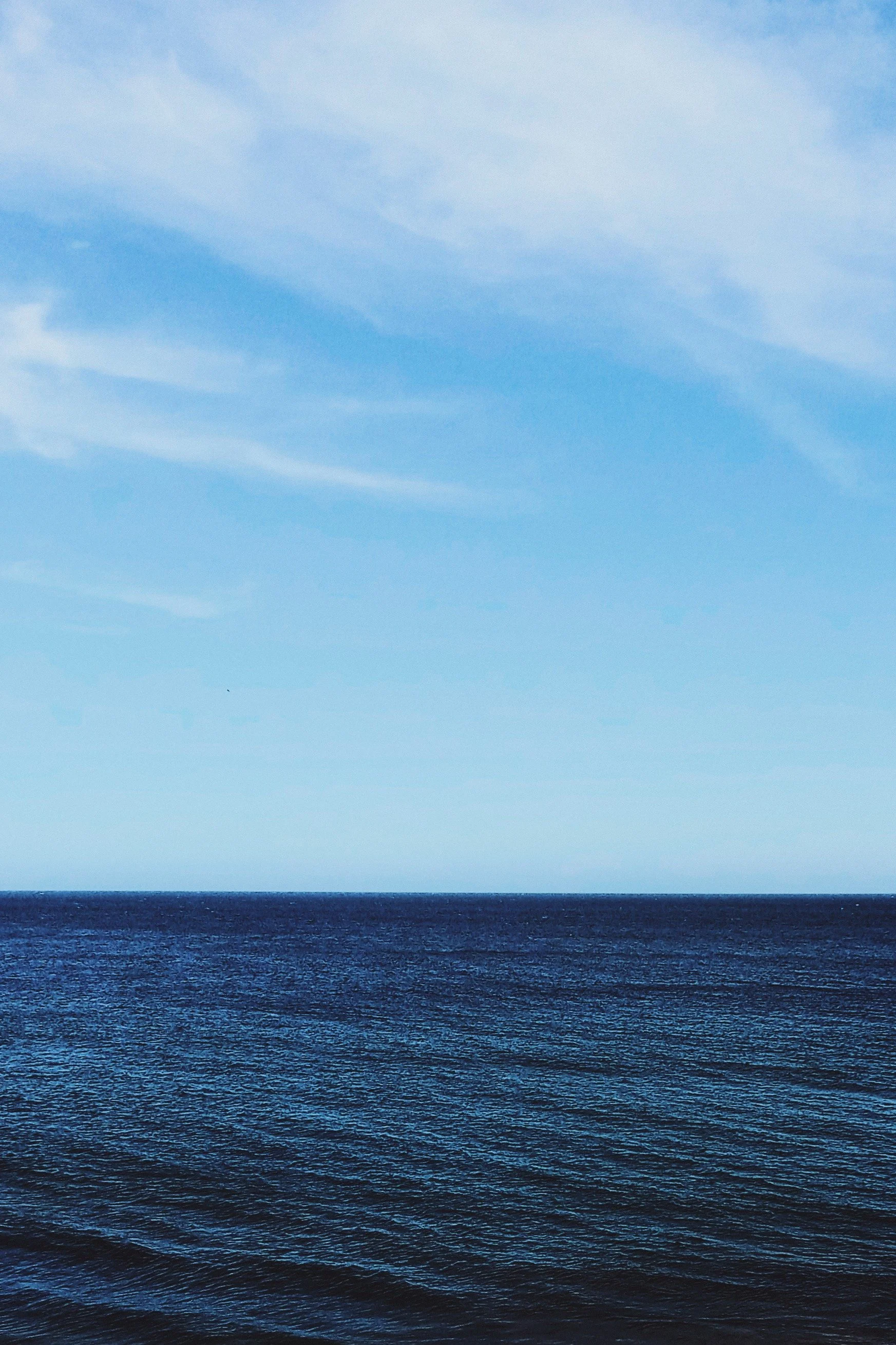 Large body of water with dark waves in the foreground and a clear, blue sky with wispy clouds above.
