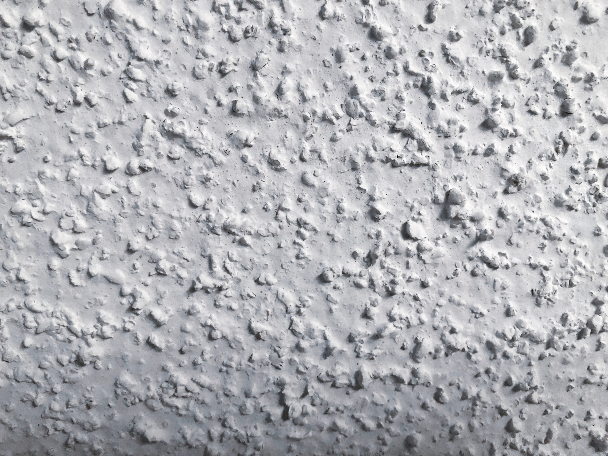 Close-up of a textured, painted white wall with small, irregular bumps and patches.