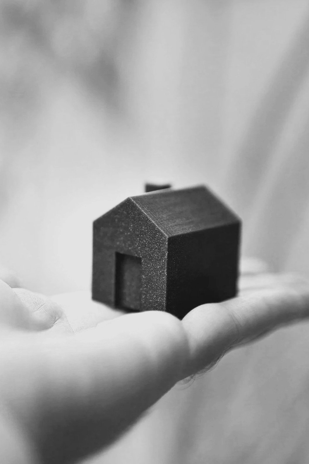 A small black house-shaped object is resting on a person's open palm, with a blurred background.