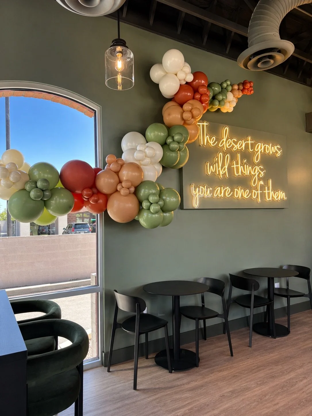 Wall balloon garland around a neon sign for Desert Drifter Coffee Shop.