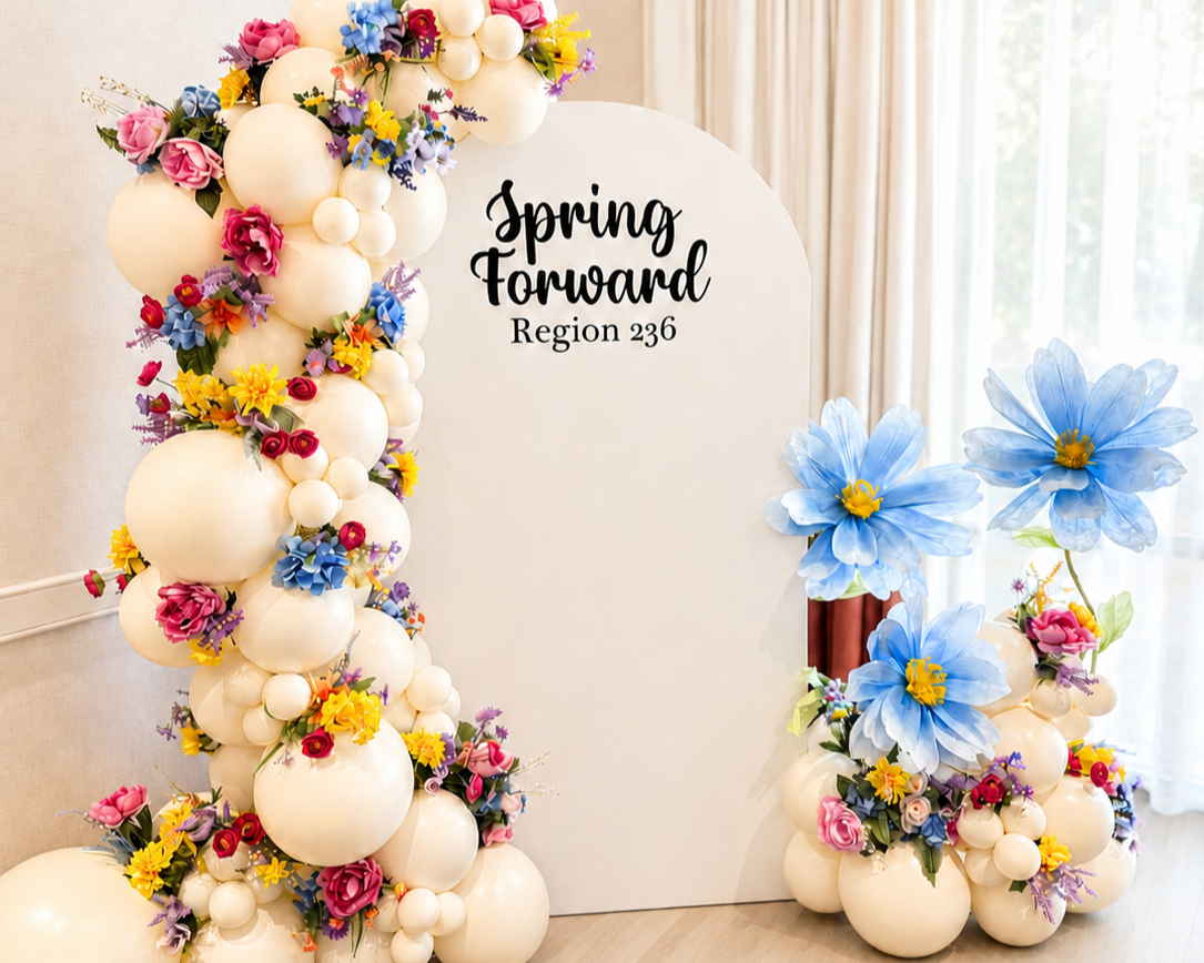 Decorative spring festival display with balloons and colorful flowers around a white backdrop that reads "Spring Forward Region 236".