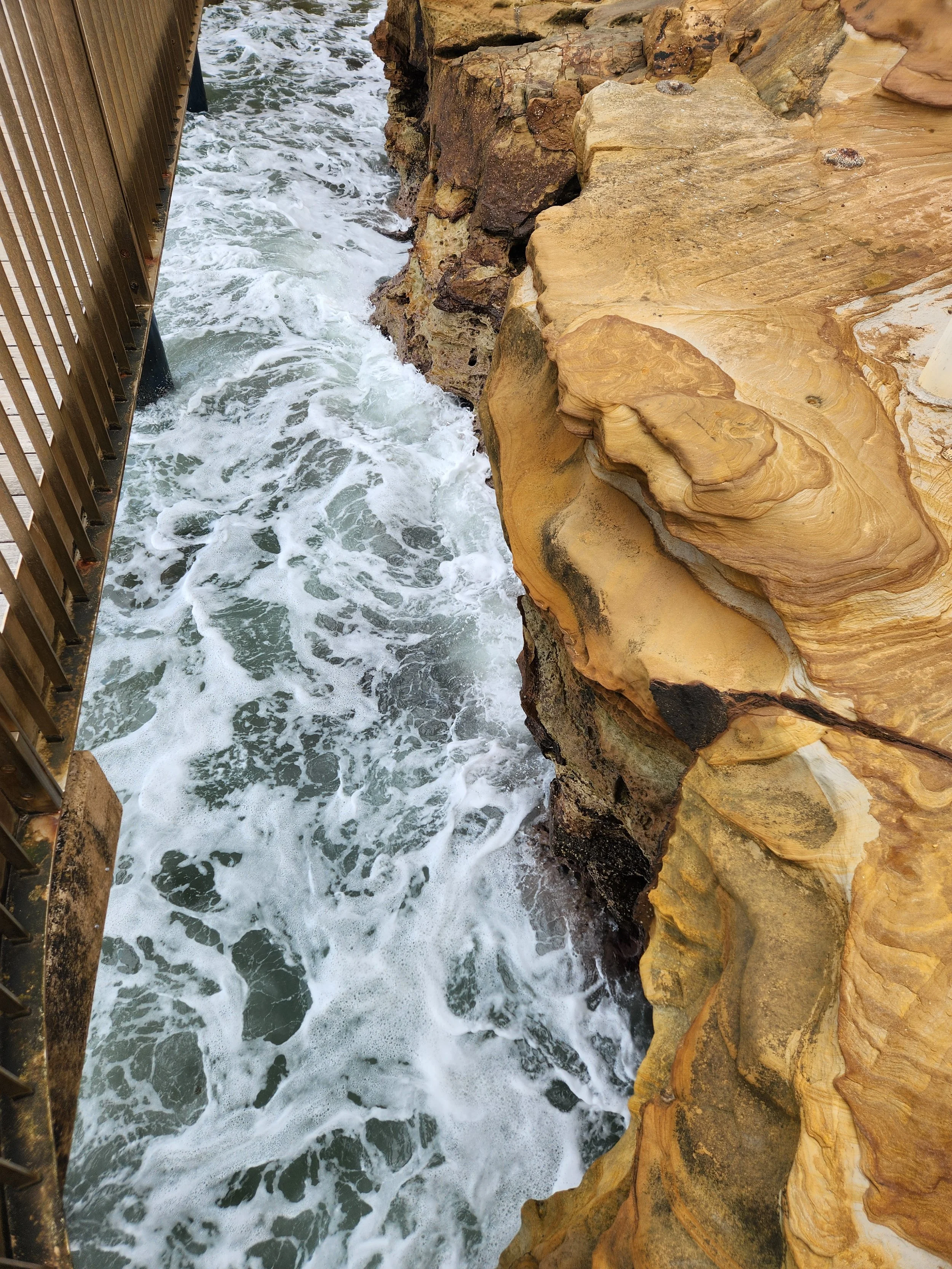 Photo of a rocky coastal cliff with water crashing against it, seen from above.