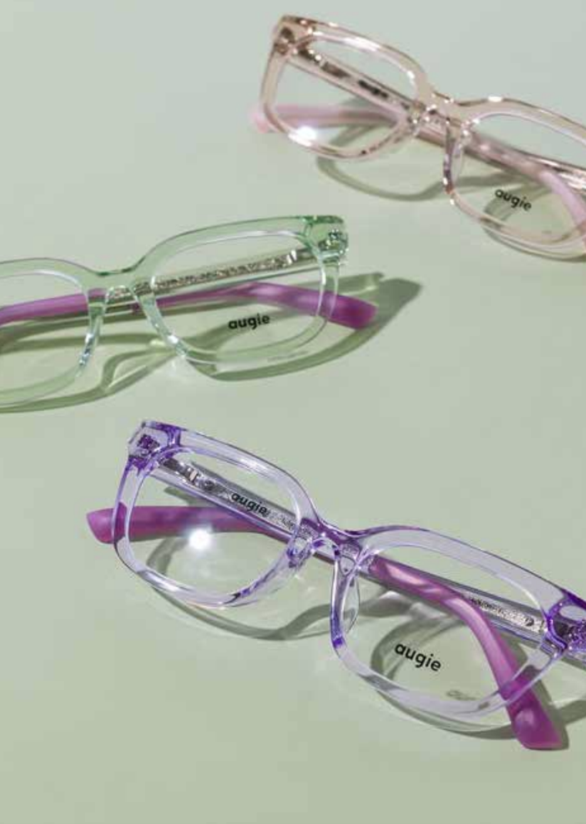Three pairs of colorful glasses with the brand name "augie" on the lenses, placed on a light green surface, casting shadows.