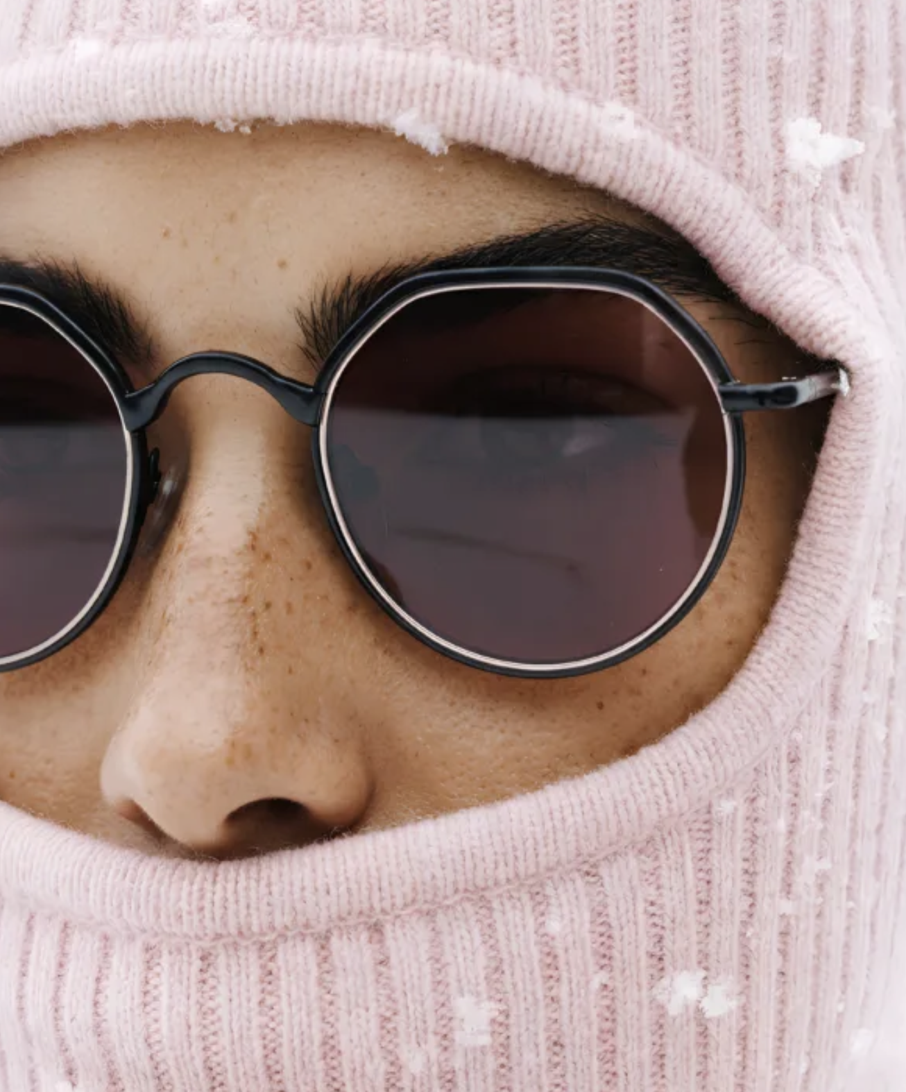 Close-up of person wearing round black sunglasses and a pink hoodie with a distressed texture.